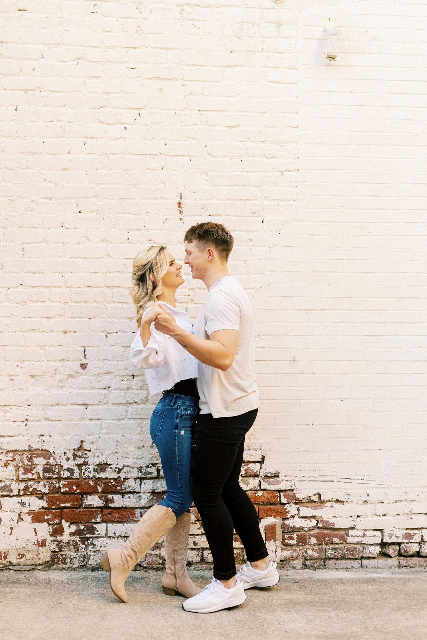 engaged couple hugs in front of white washed wall in Downtown Concord