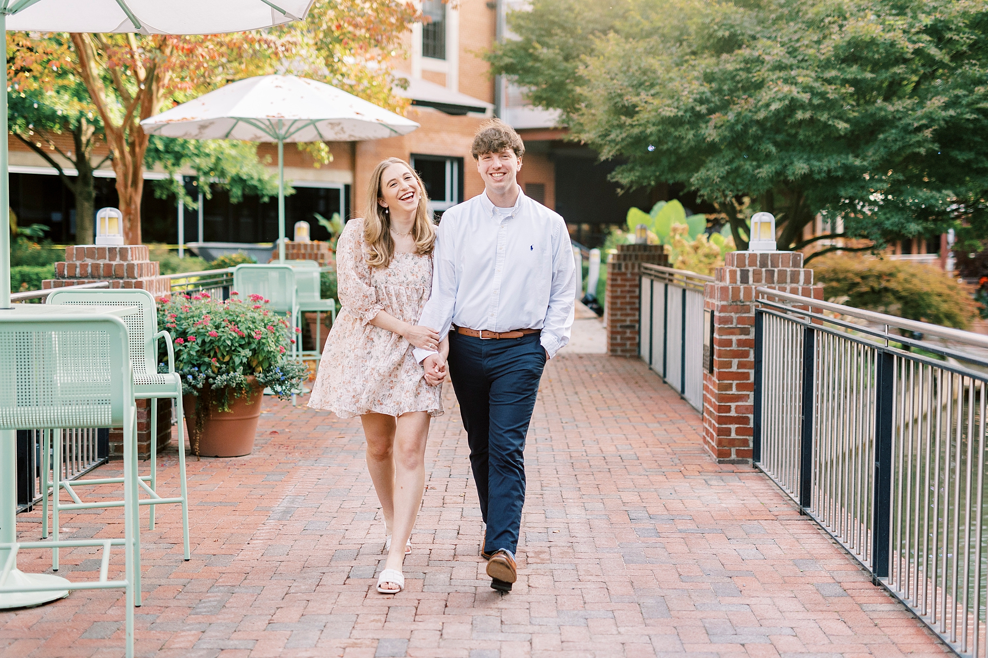 engaged couple holds hands walking long brick pathway at American Tobacco Campus