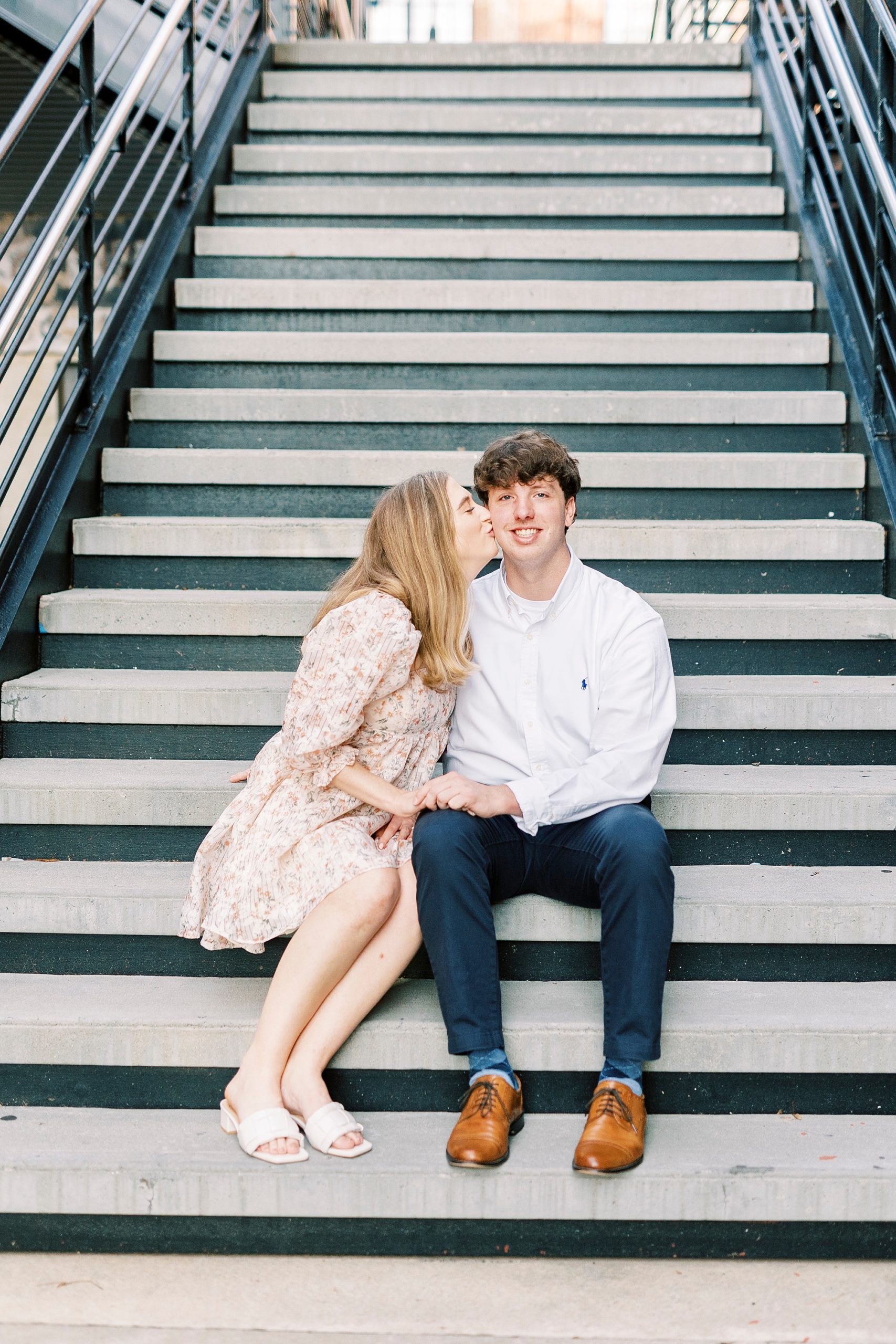 woman leans to kiss fiancee's cheek sitting on steps in Durham NC