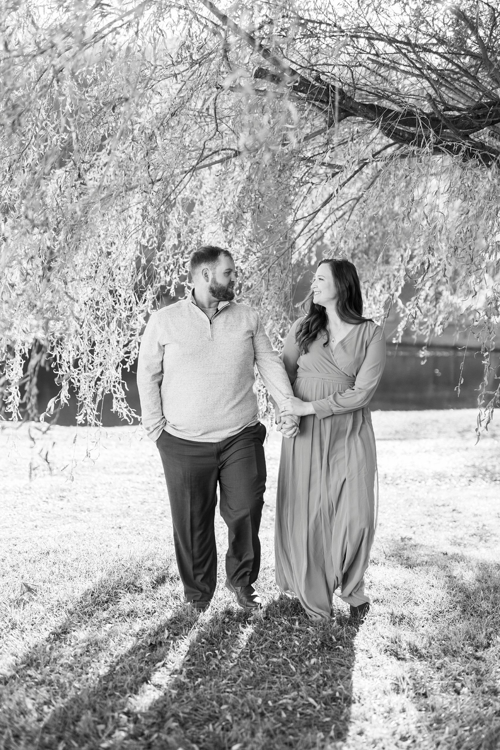 engaged couple walks holding hands under willow tree at Chetola Resort