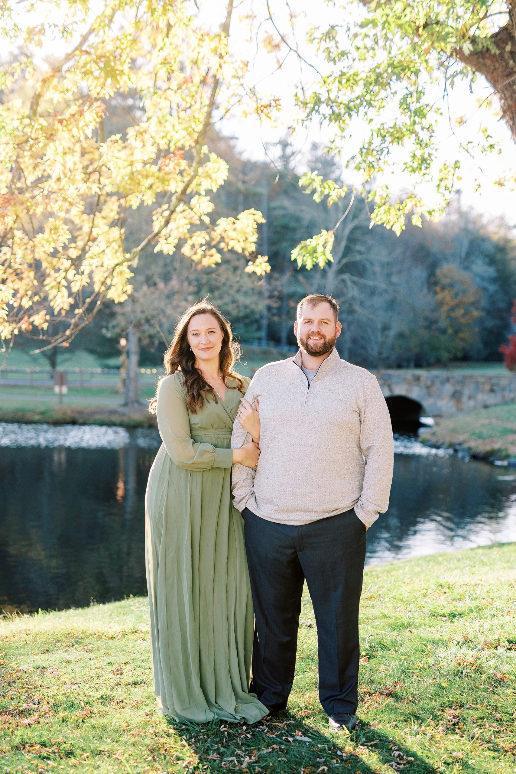 engaged couple stands together under tree along water at Chetola Resort