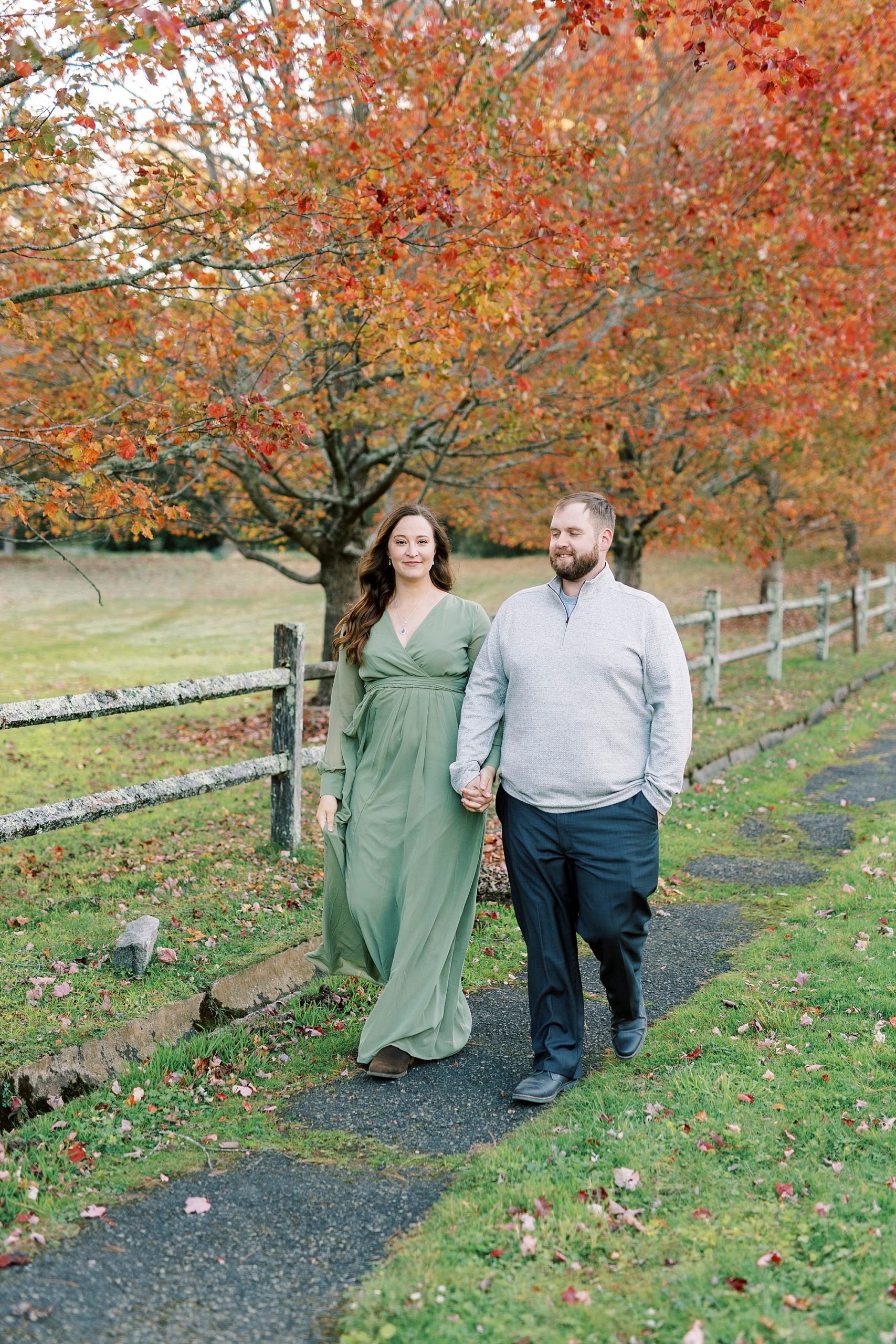 engaged couple walks by wooden fence and red leaves at Chetola Resort