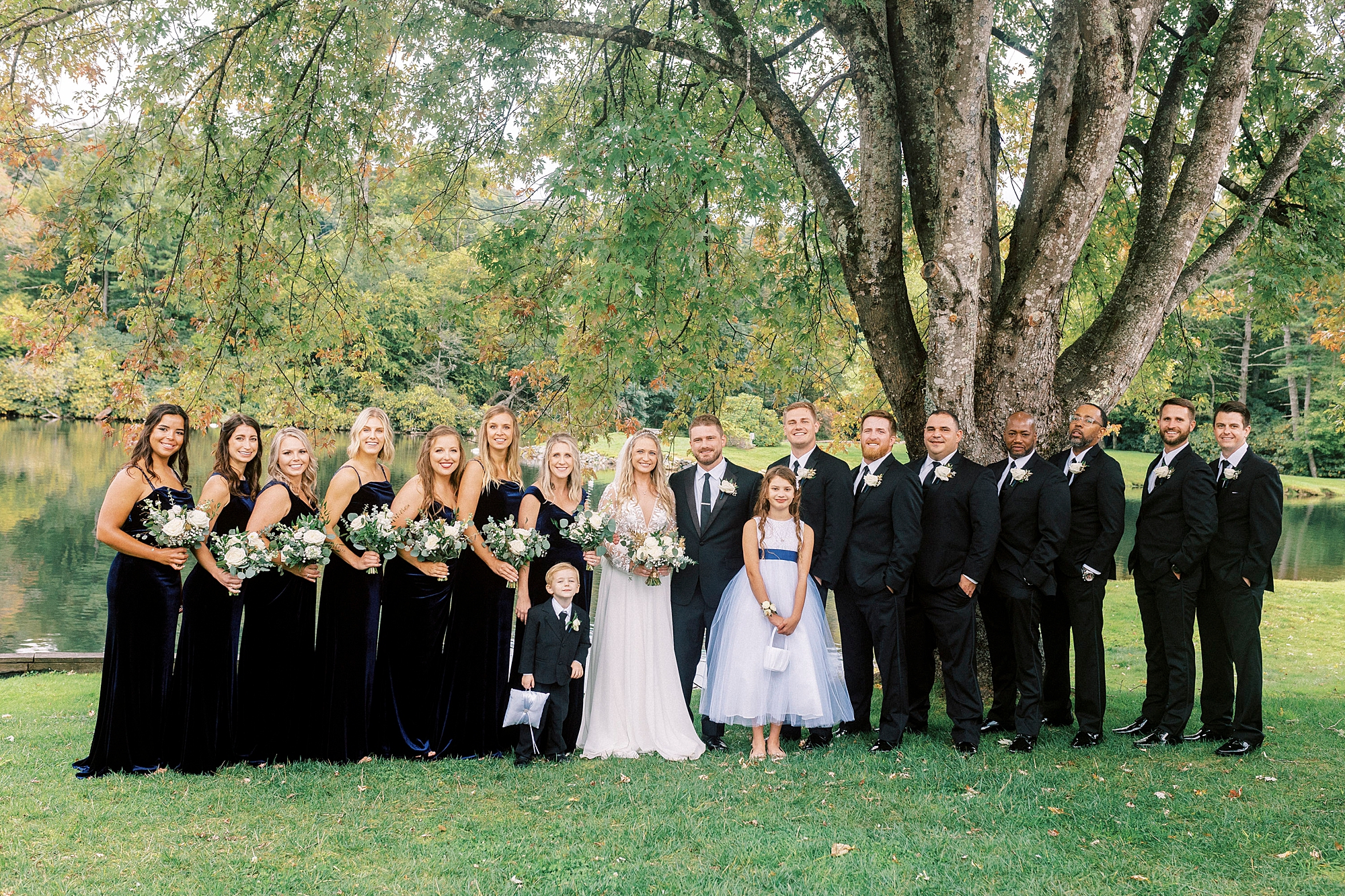 bride and groom stand with wedding party in black under tree at Chetola Resort