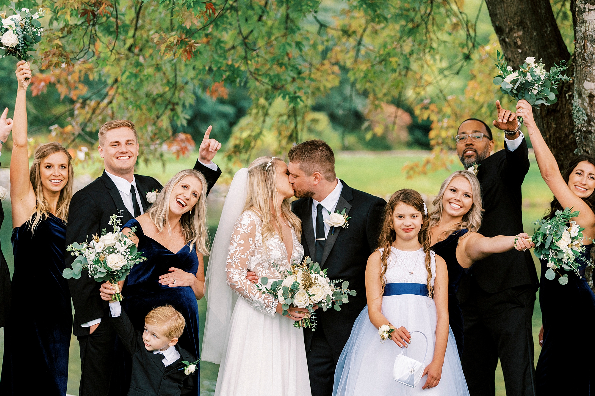 bride and groom kiss with wedding party cheering during fall wedding at Chetola Resort