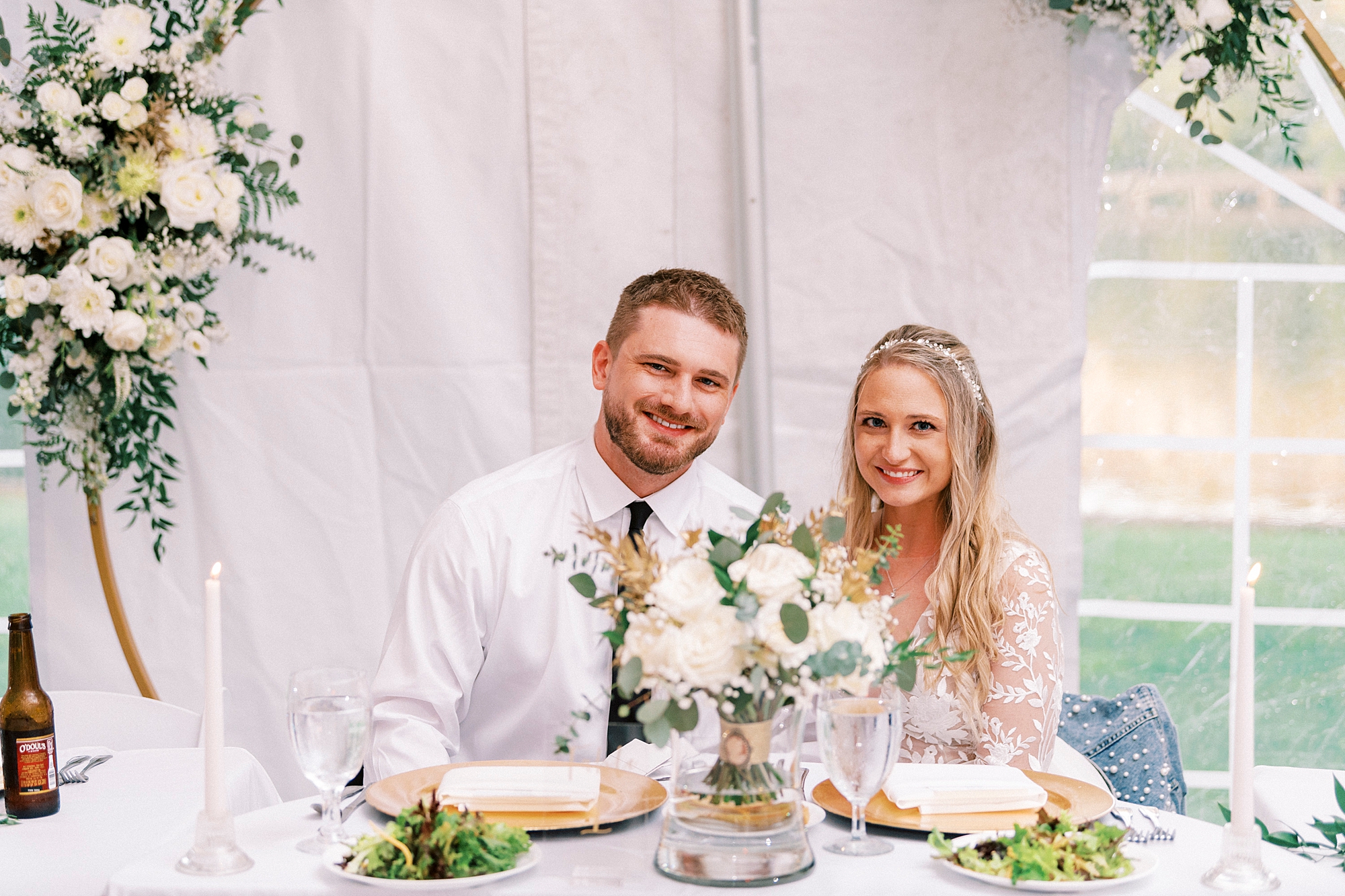 bride and groom sit together at sweetheart table under golden arbor at Blowing Rock NC wedding reception