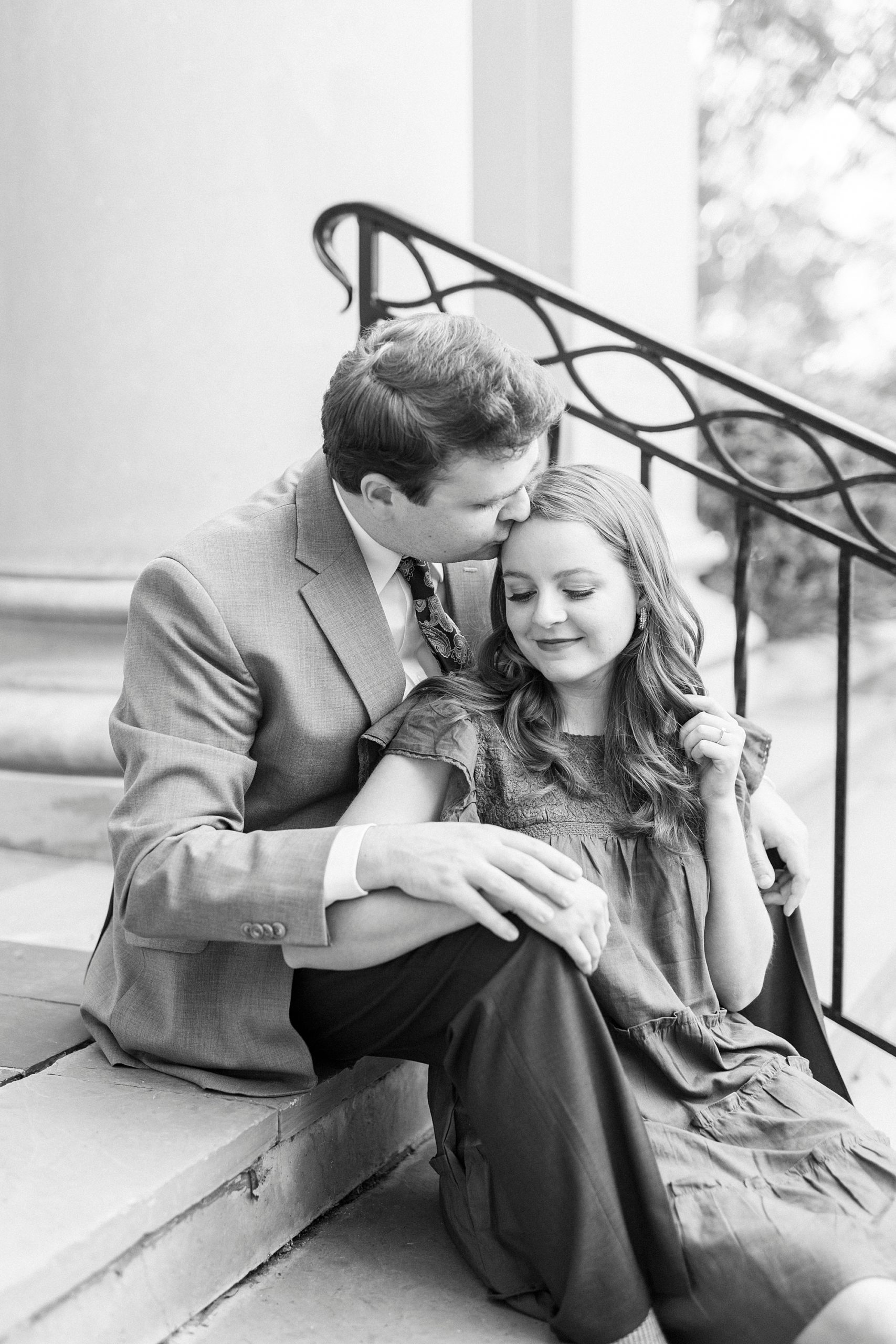 groom leans to kiss bride's forehead while she sits between his knees