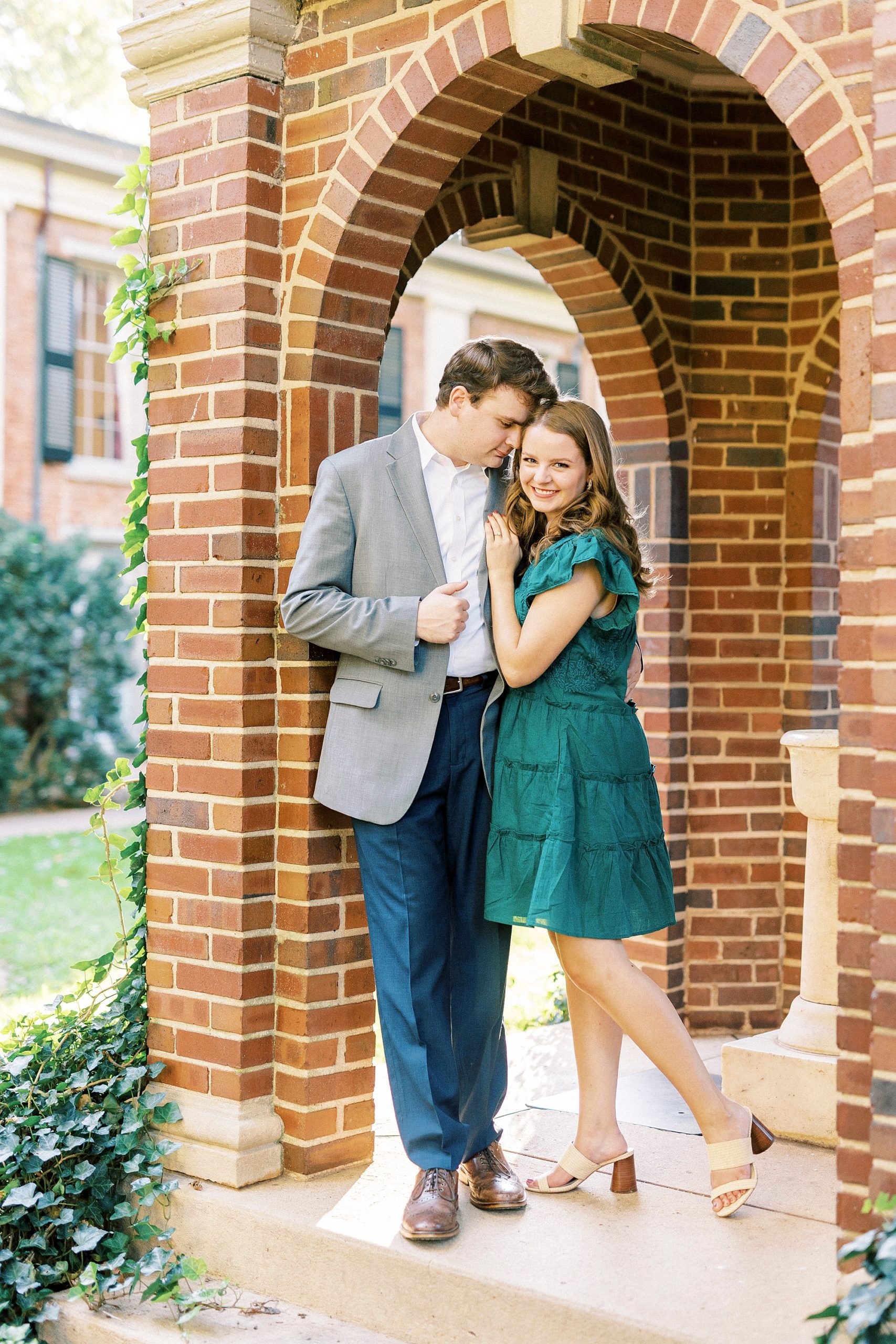 bride in green dress hugs against brick column in Downtown Davidson