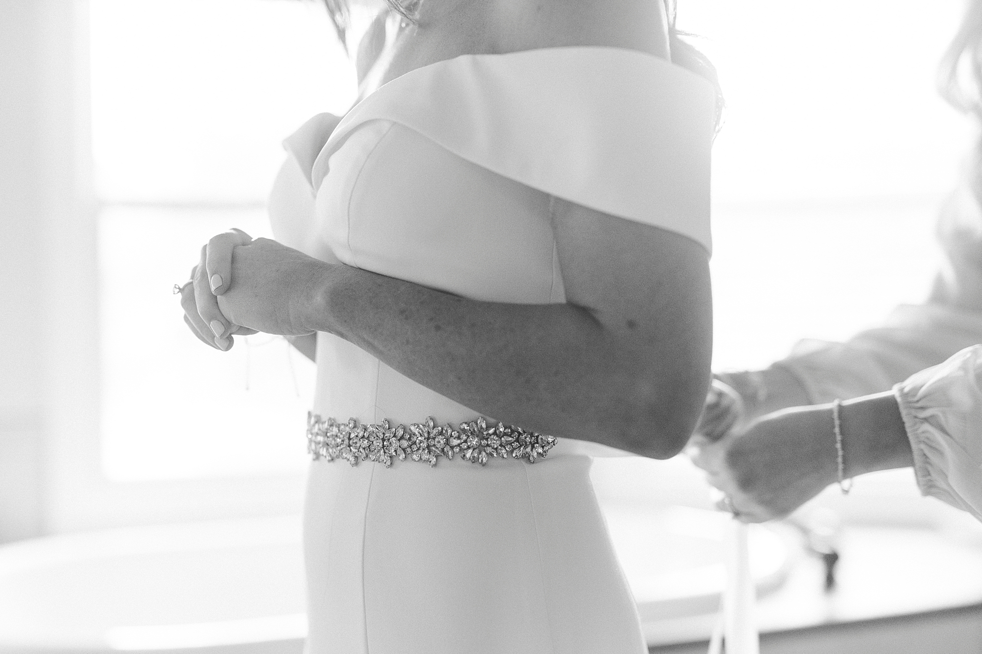 bride in off-the-shoulder gown gets ribbon tied around waist