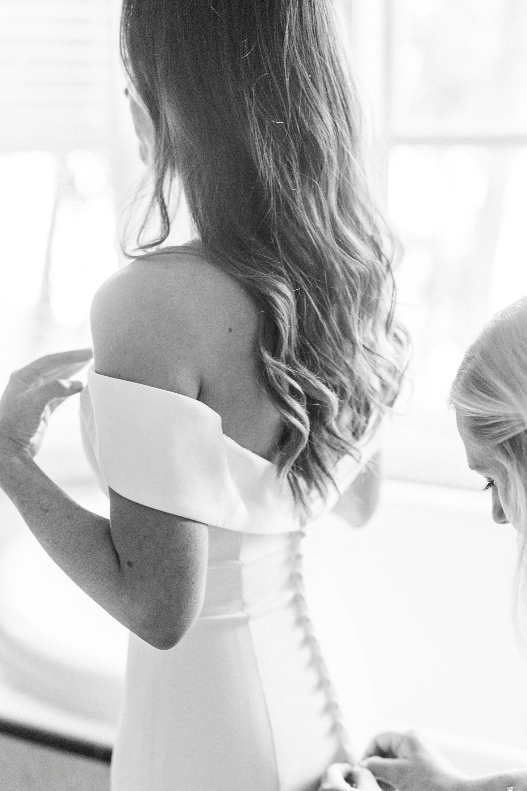 mother helps bride with buttons on wedding gown