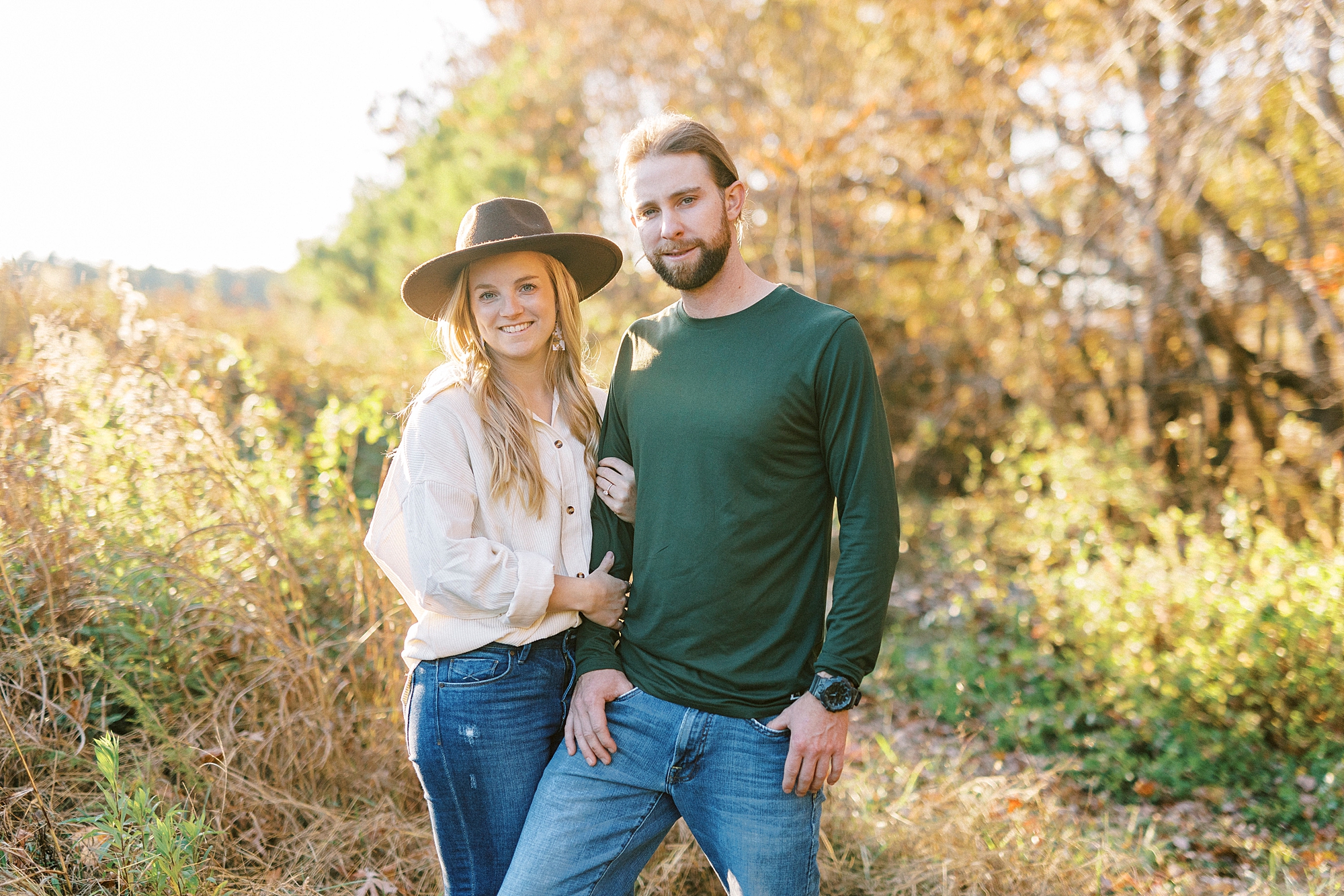 engaged couple stands together with bride holding groom's arm during fall engagement photos
