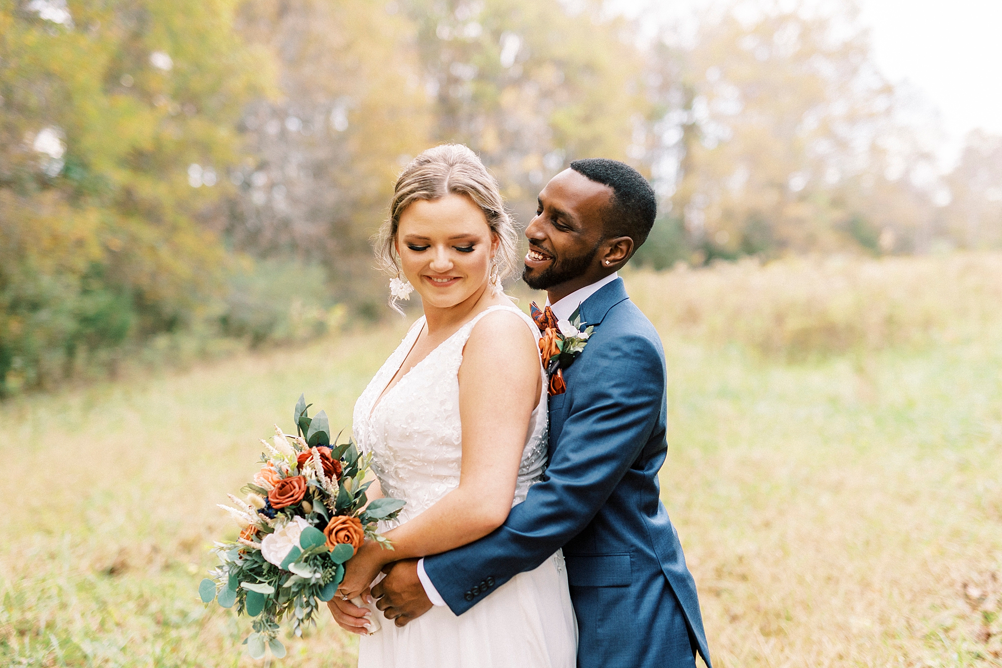 groom hugs bride during fall wedding portraits in meadow