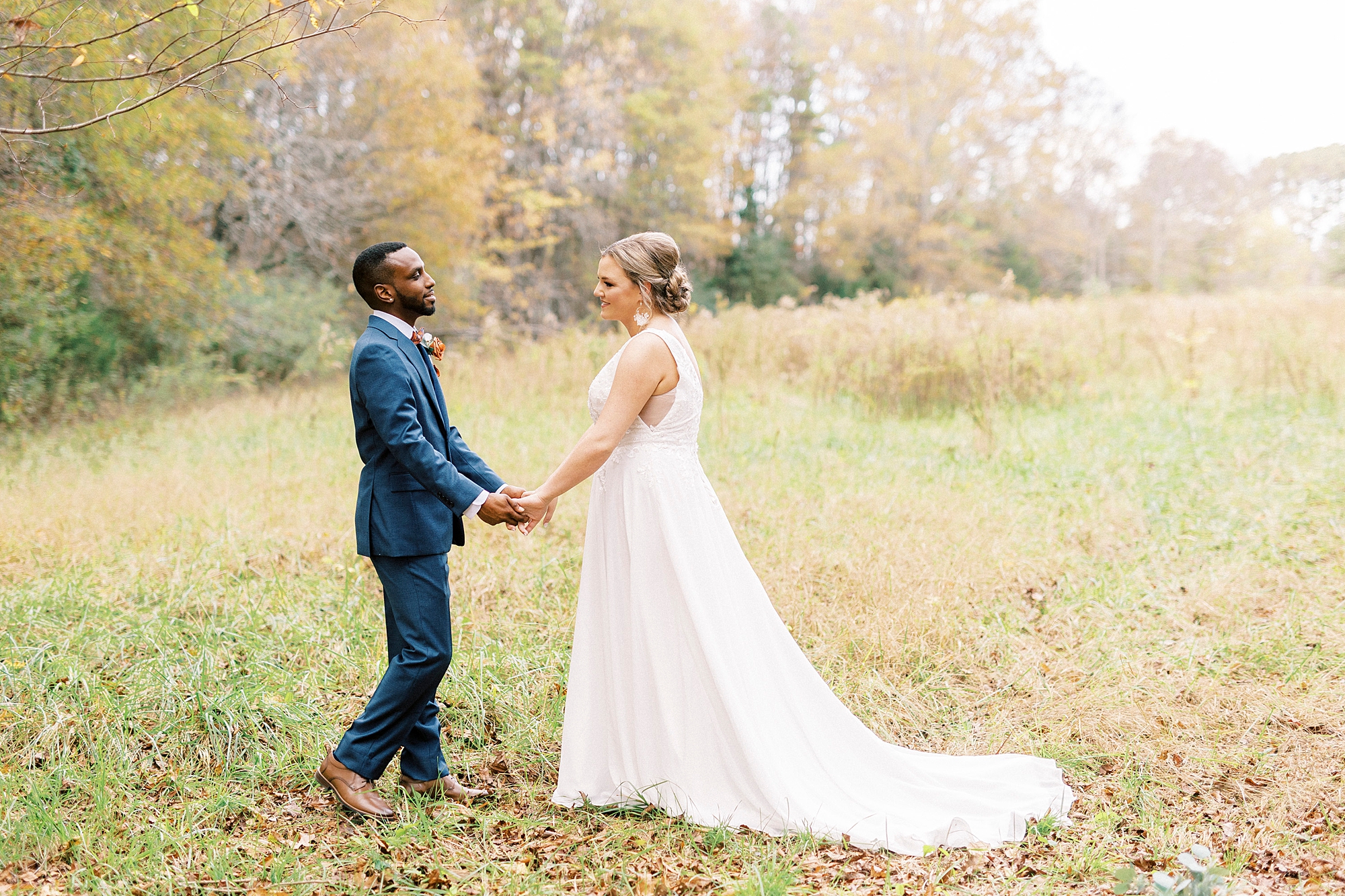 groom holds bride's hand leading her across meadow 