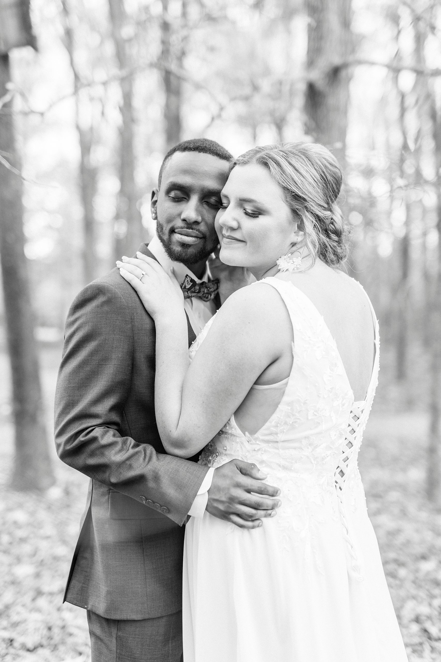 bride and groom hug cheek-to-cheek in fallen leaves 