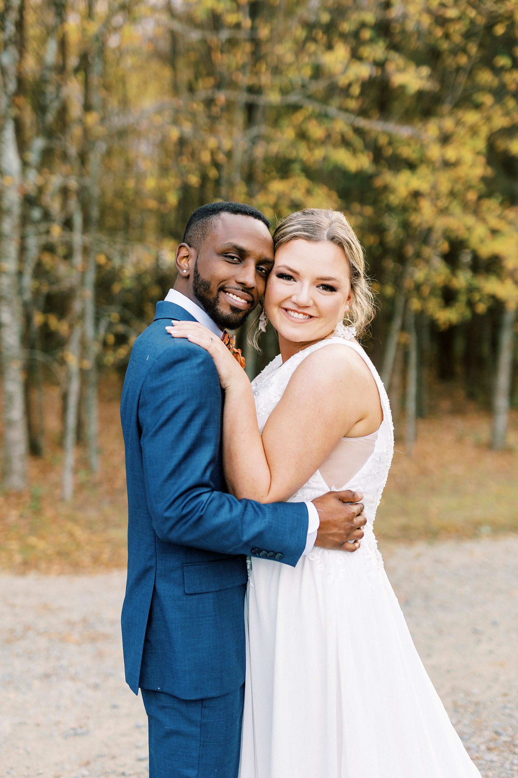 bride and groom hug together on walkway with yellow trees behind them 