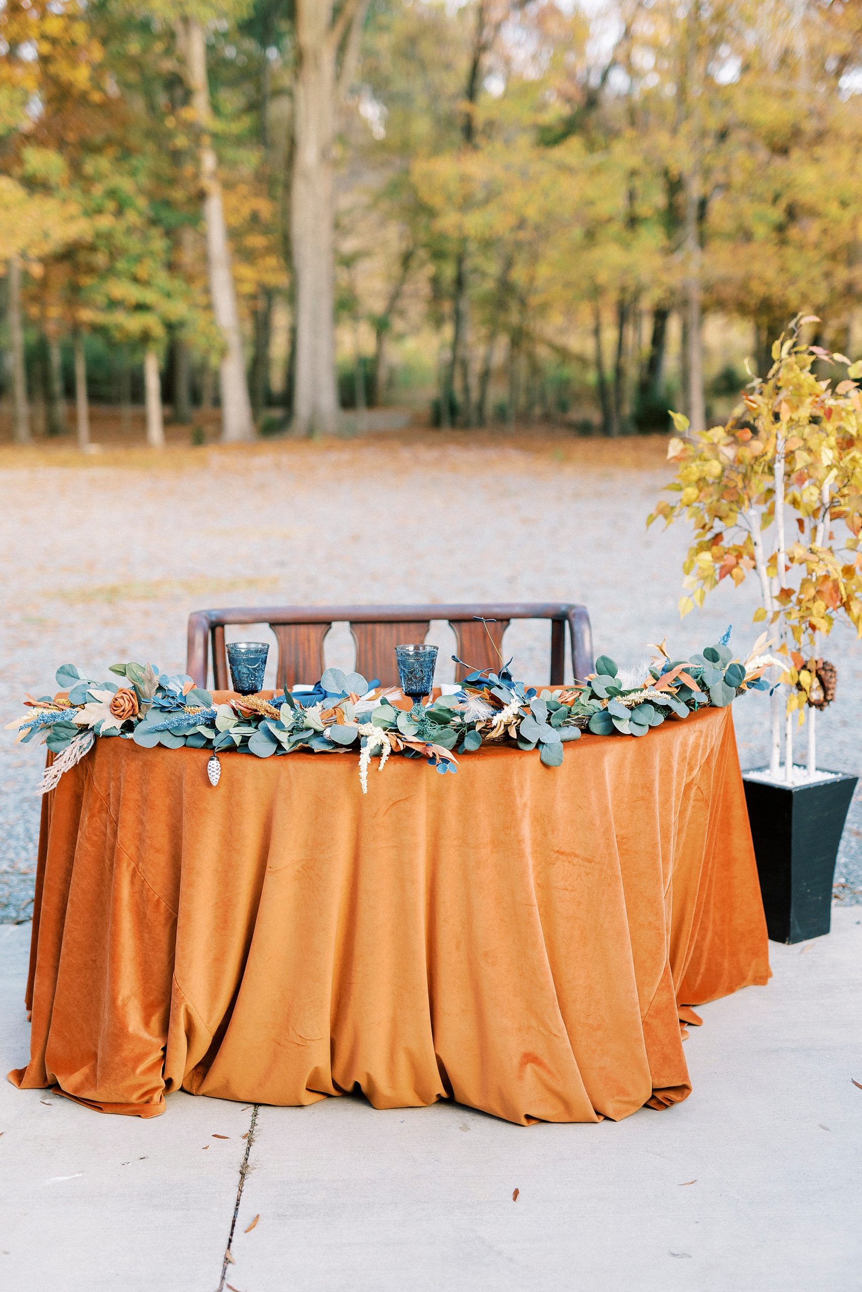sweetheart table with orange table cloth and greenery 