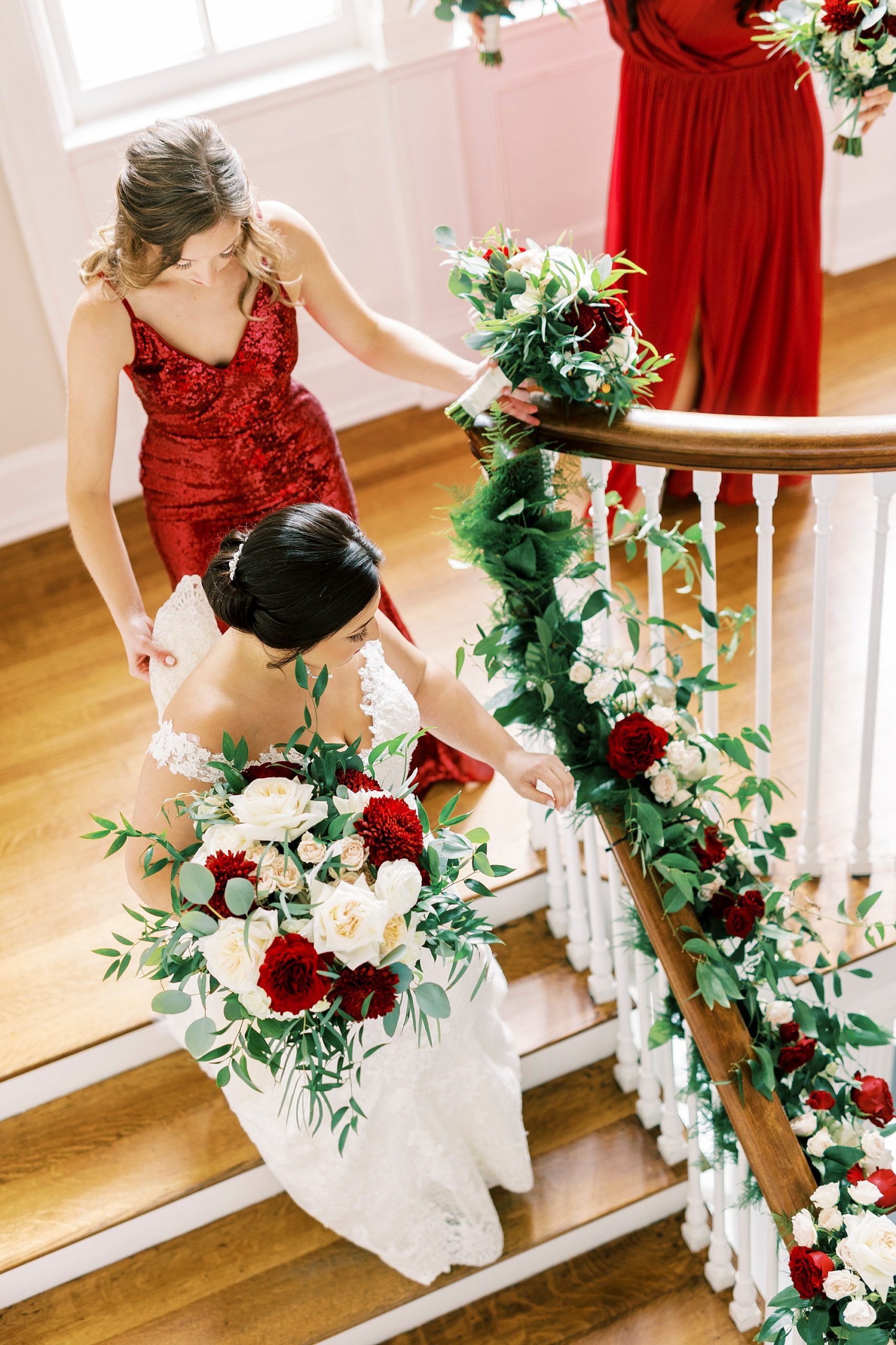 bridesmaids in red gowns walk down steps at Separk Mansion with bride
