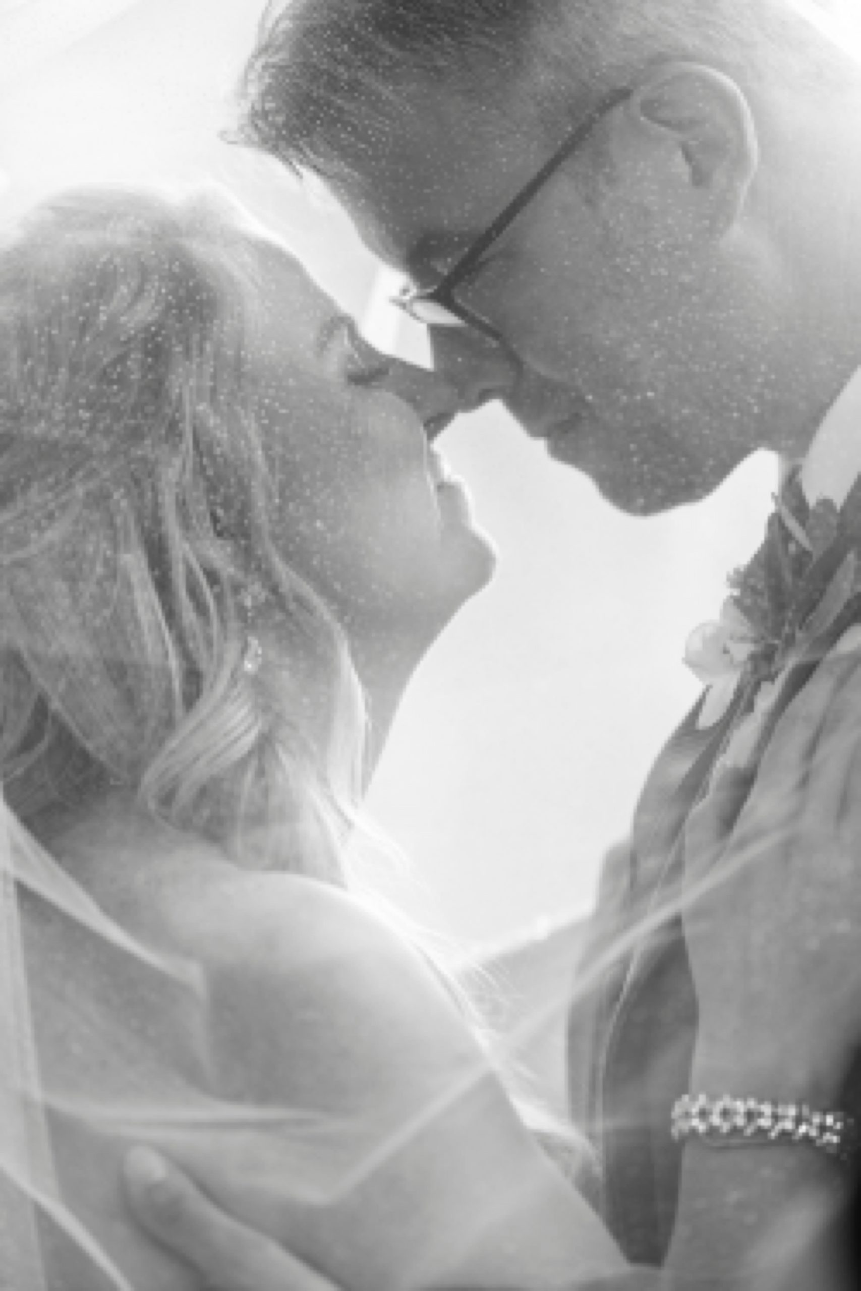 bride and groom touch noses under bride's veil in black and white photo