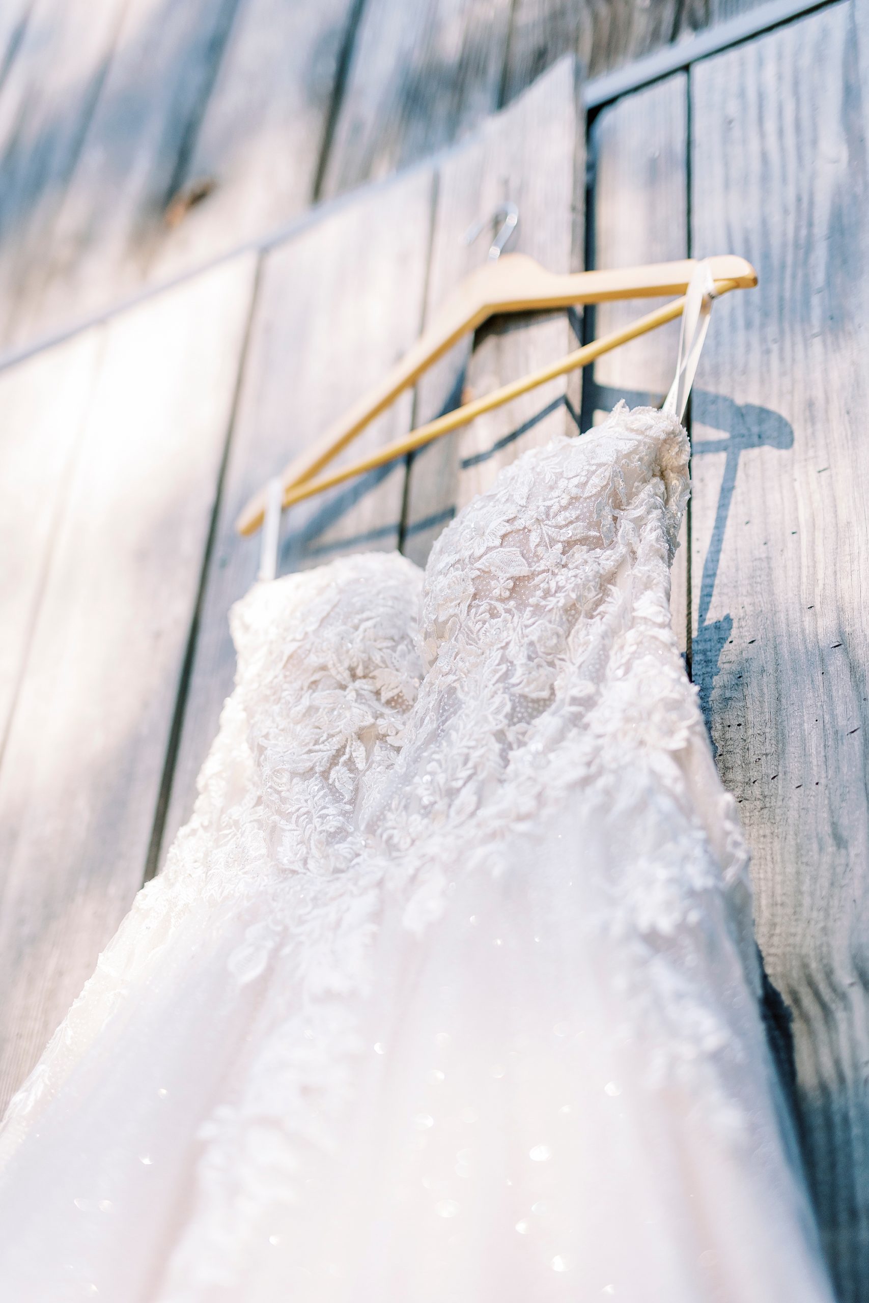 wedding dress hangs on wooden wall of barn at the Gin at Aw Shucks Farm