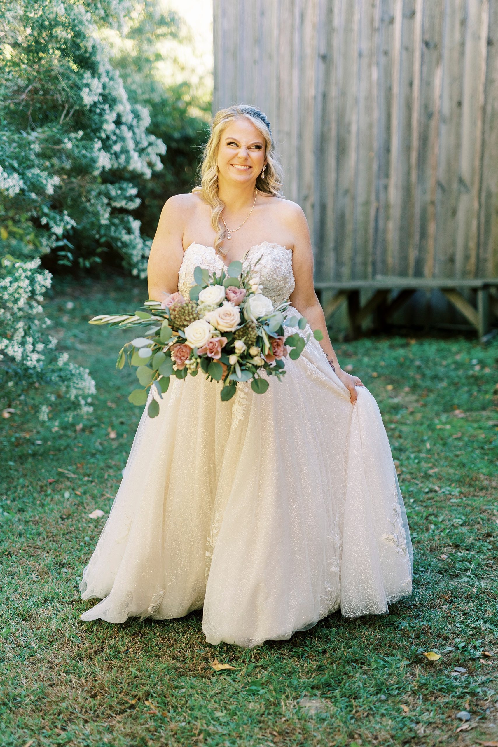 bride walks moving skirt of wedding dress holding bouquet of pink and white flowers