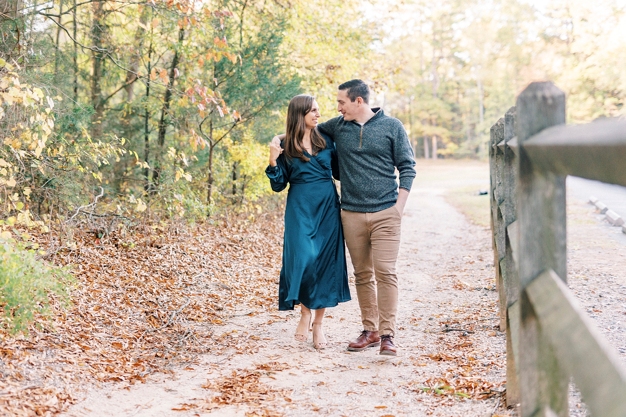 engaged couple walks through fallen leaves along path at Latta Nature Preserve