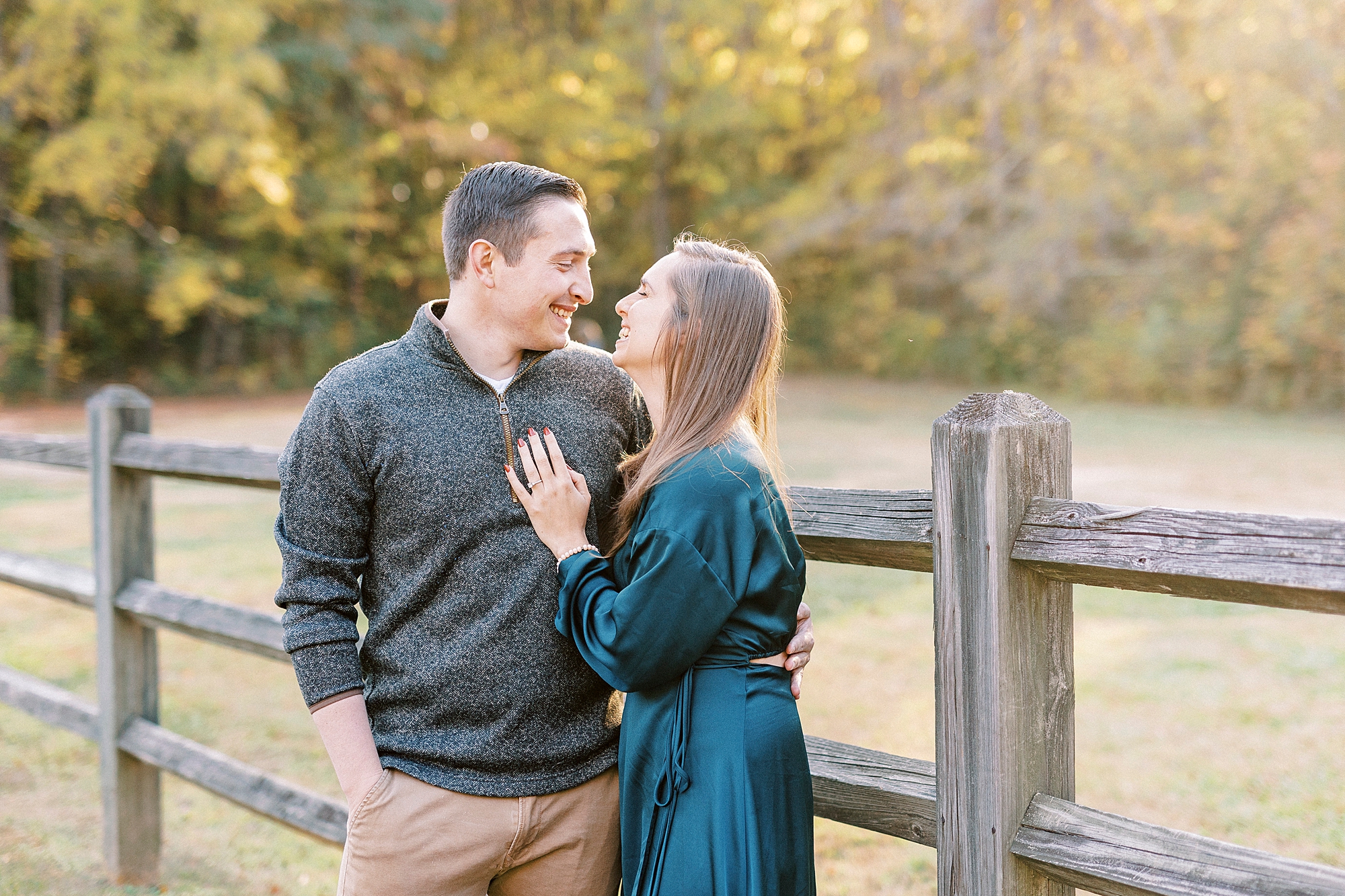 woman in teal dress looks up at man in grey sweater along wooden fence