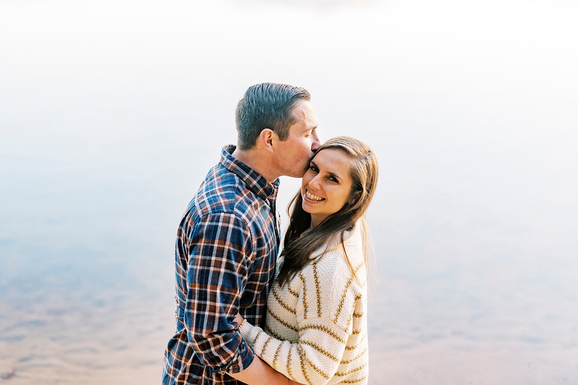 groom kisses bride's forehead in front of pond at Latta Nature Preserve