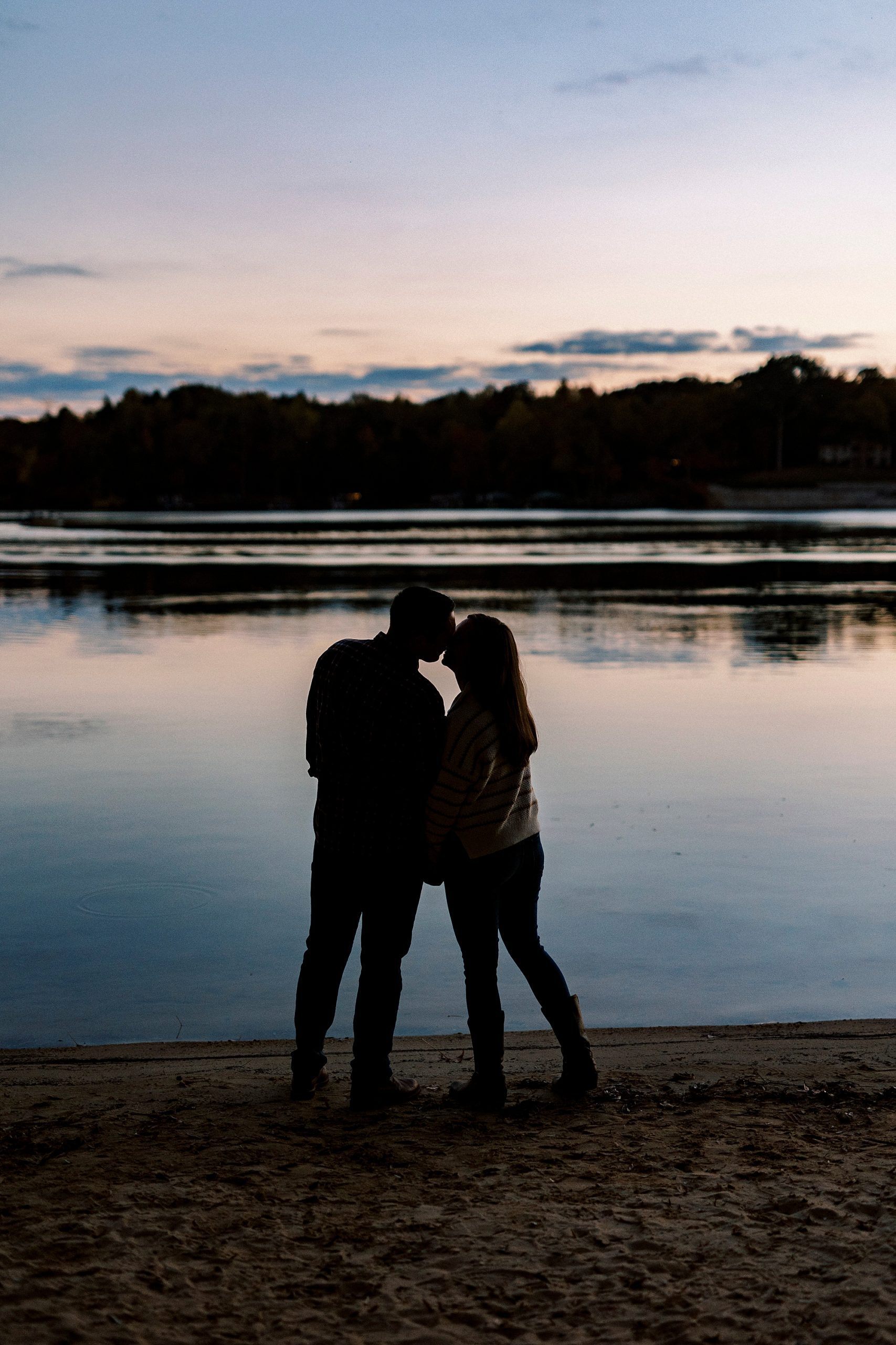 bride and groom kiss along lakefront at sunset