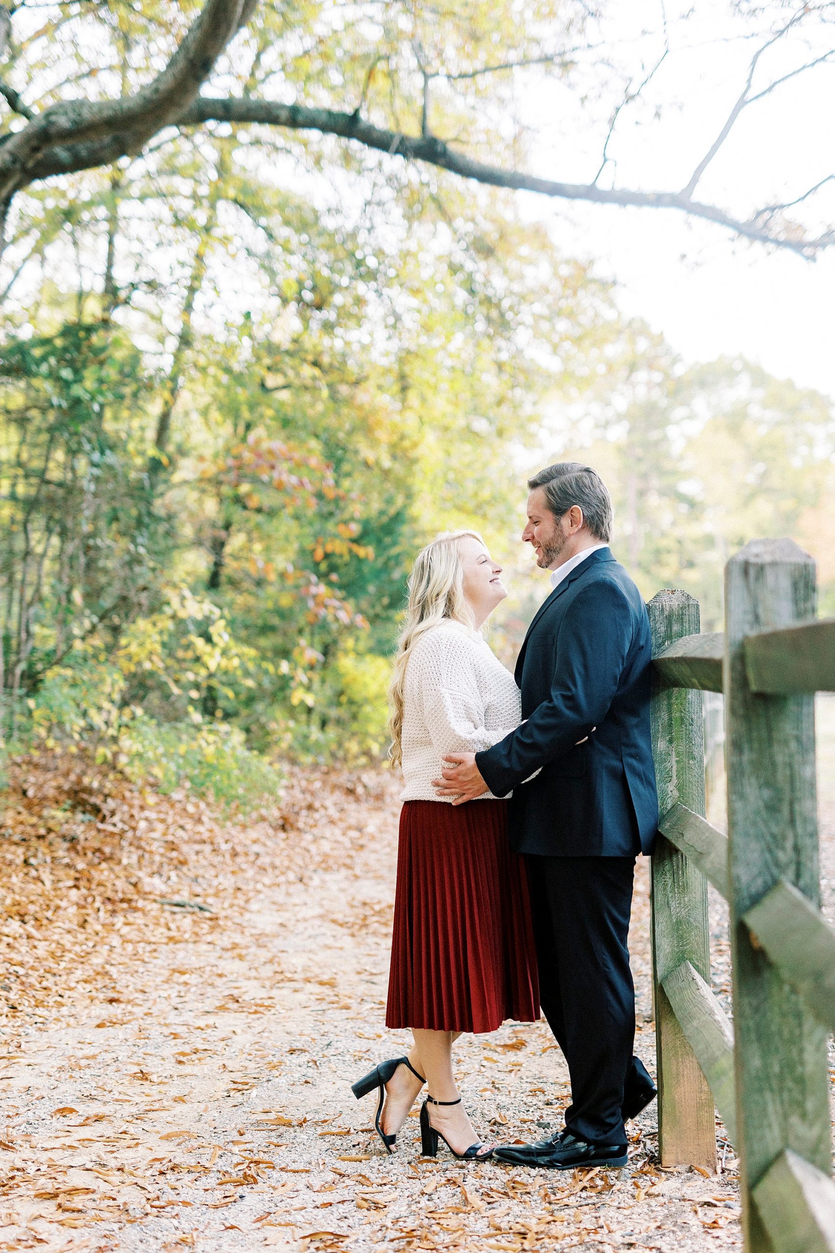 bride and groom lean against wooden fence in fall outfits