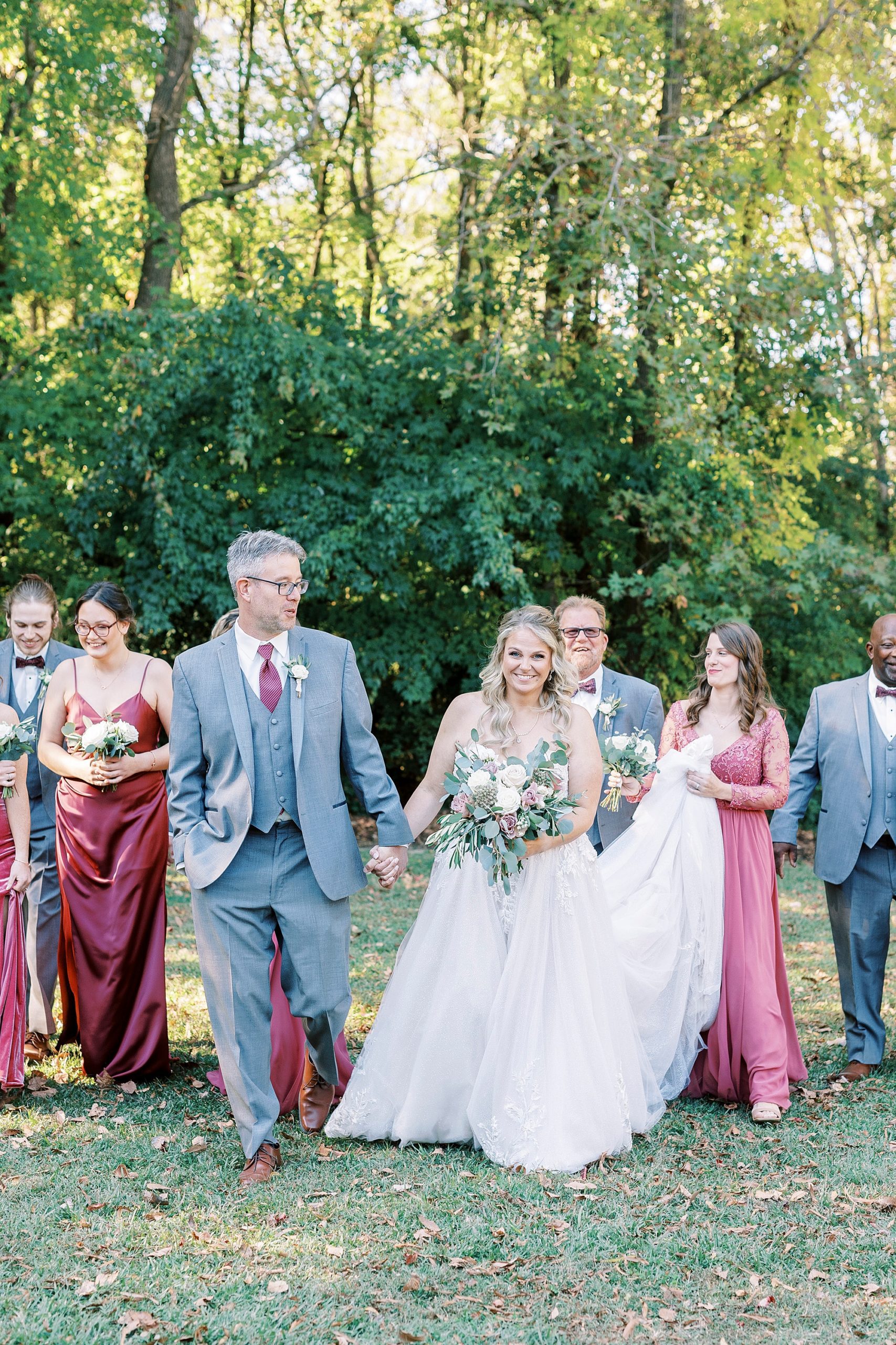 bride and groom walk with wedding party in grey and pink behind them