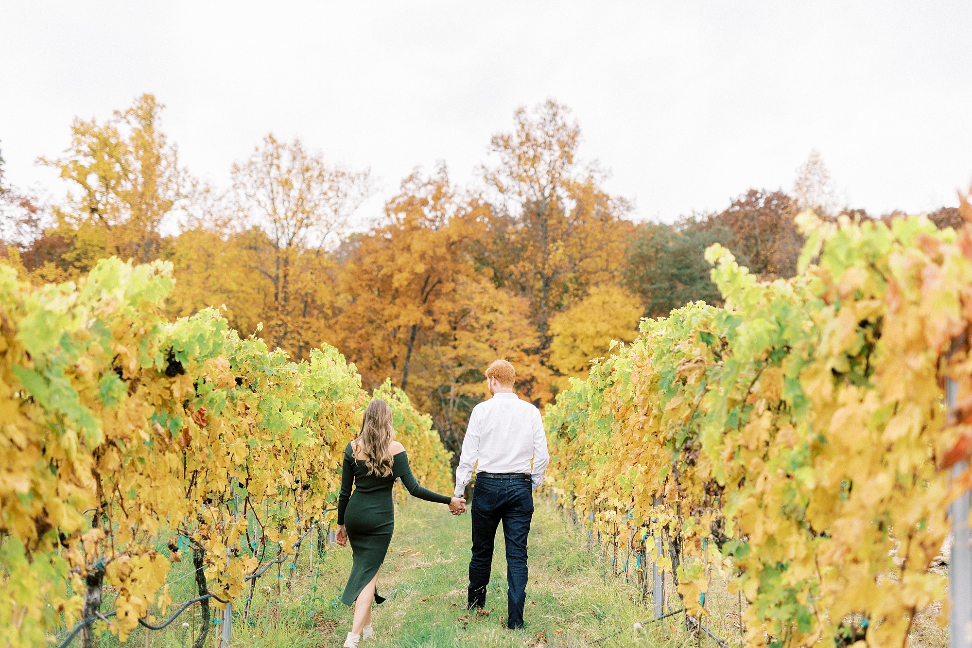 engaged couple holds hands walking through vines at Raffaldini Vineyards