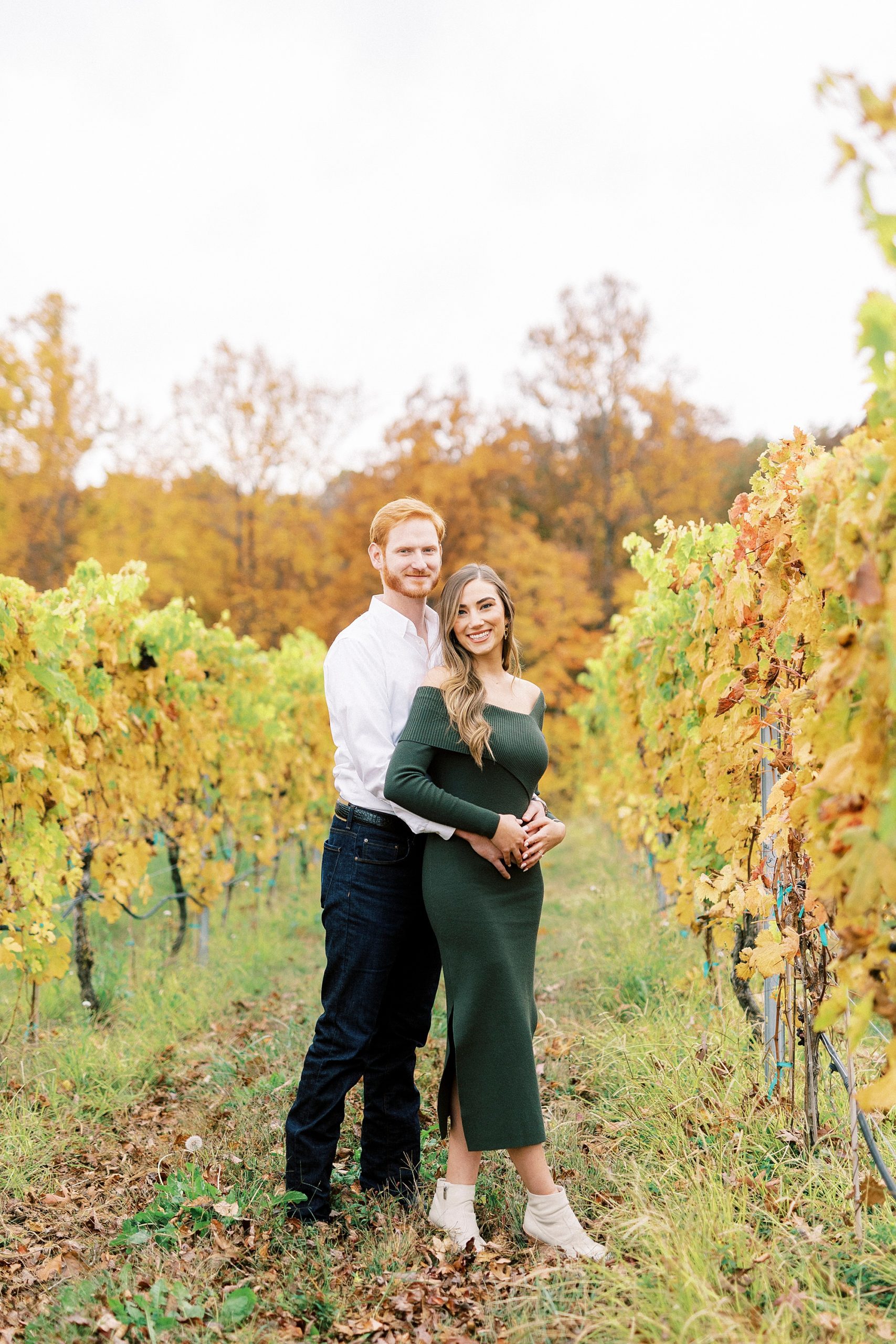 groom stands behind bride in green dress between vines 