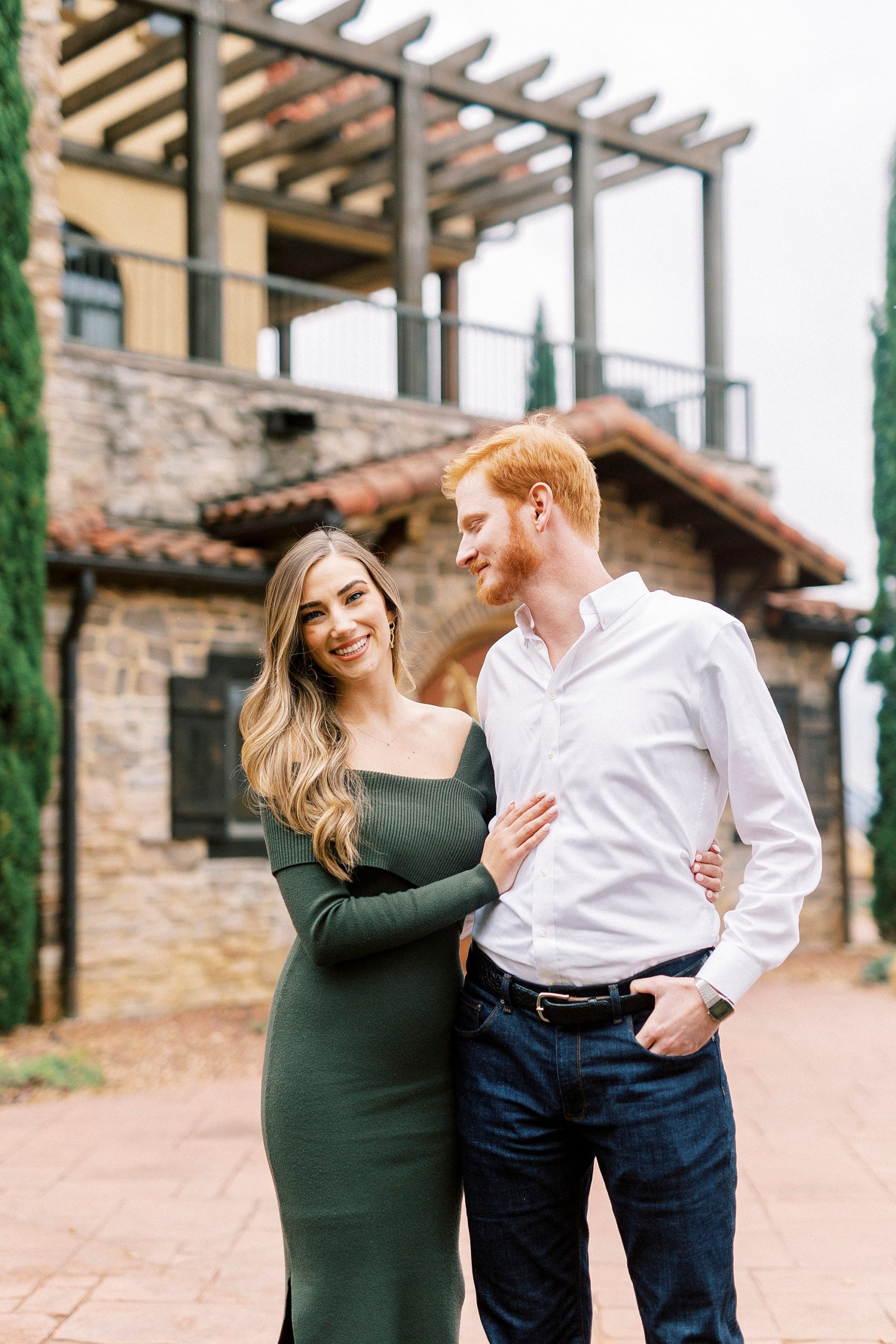 man looks over at fiancee during portraits in courtyard of Raffaldini Vineyards