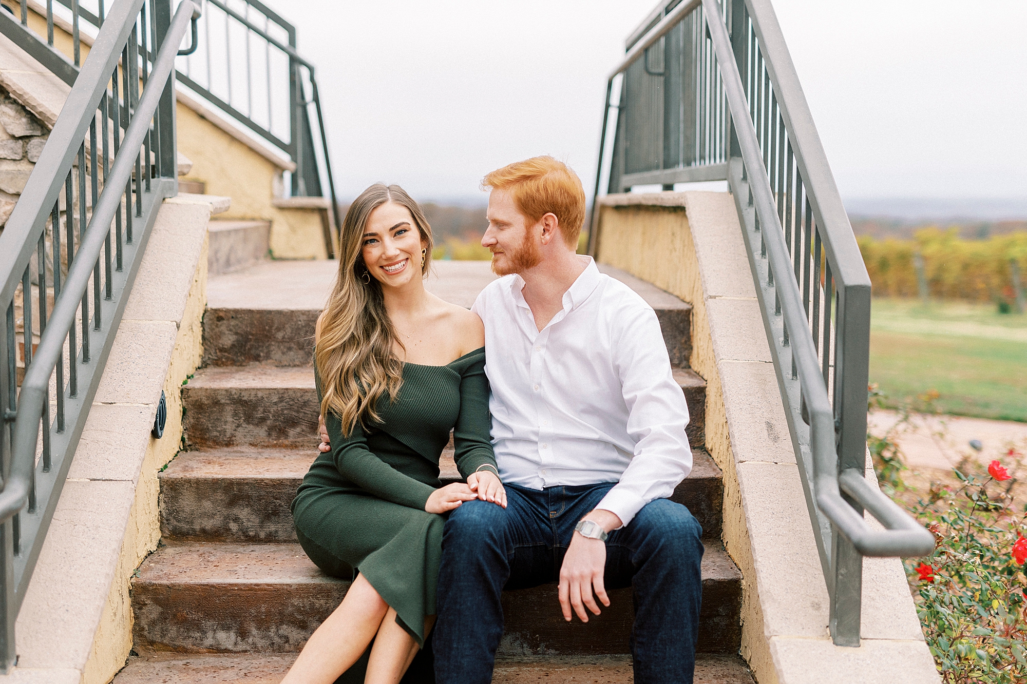 man looks at fiancee during engagement session at Raffaldini Vineyards sitting on steps 