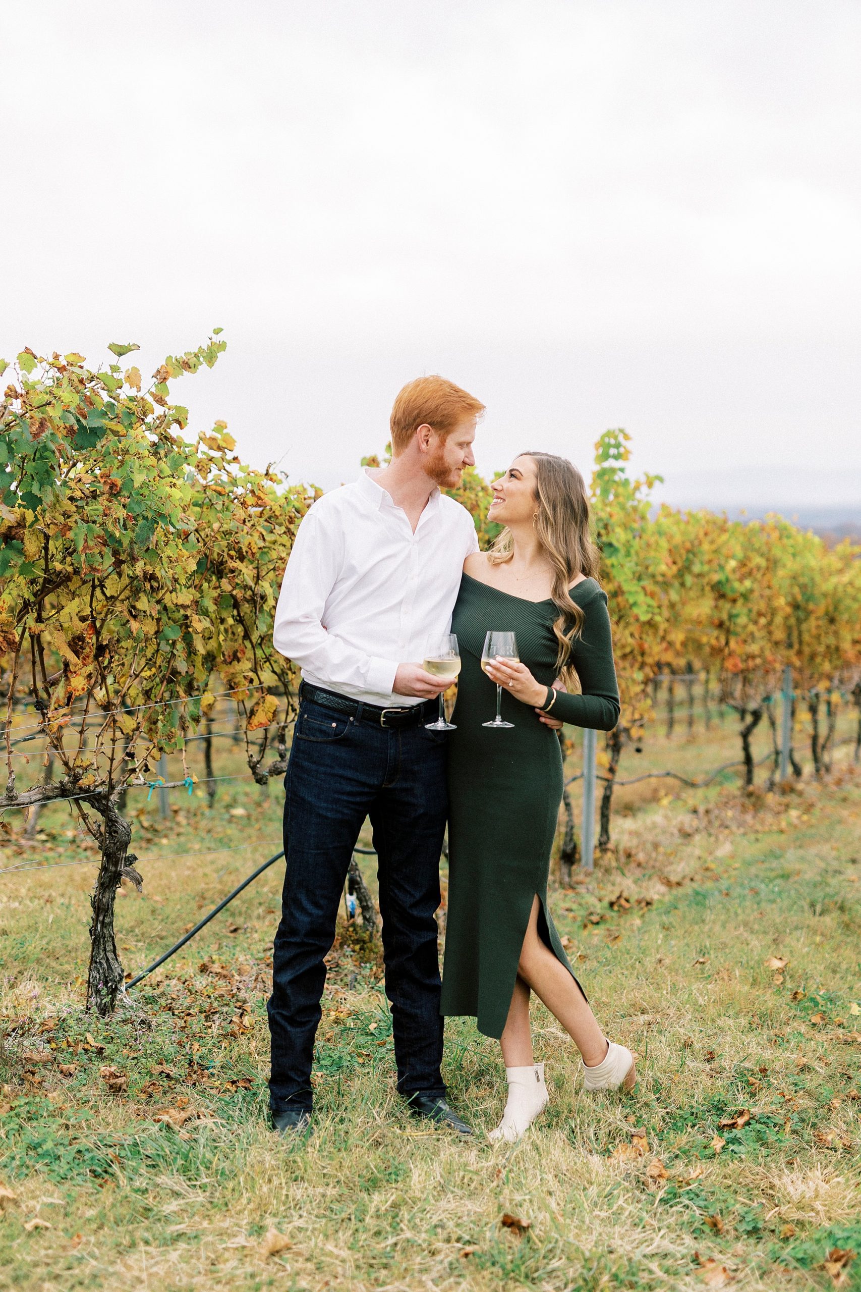 woman leans into fiancee holding glass of white wine at Raffaldini Vineyards