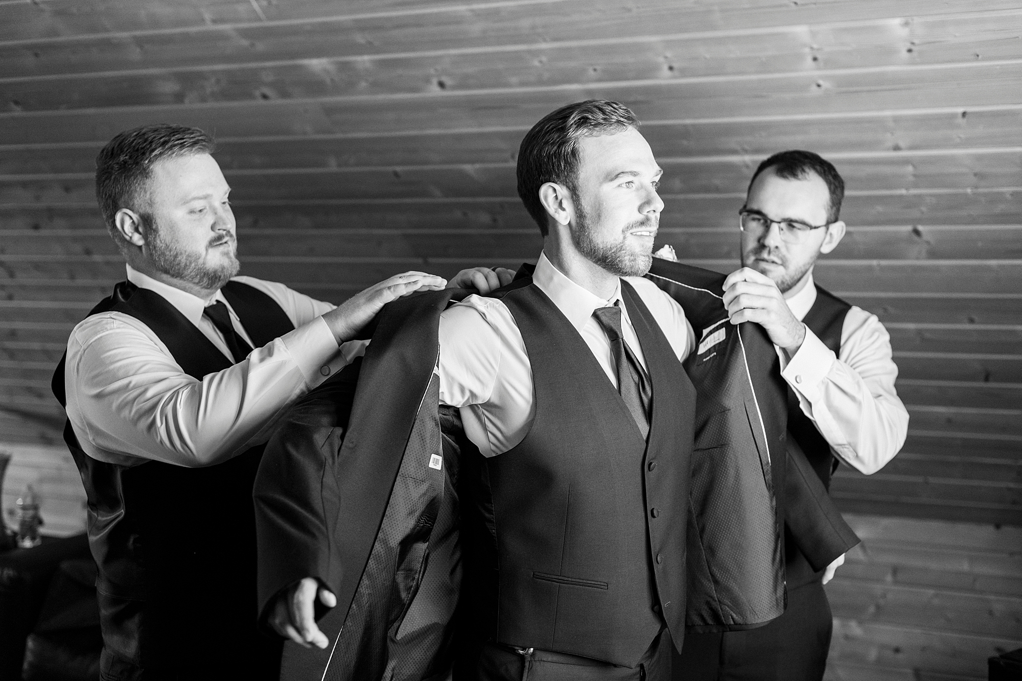 groomsman and father help groom into jacket 