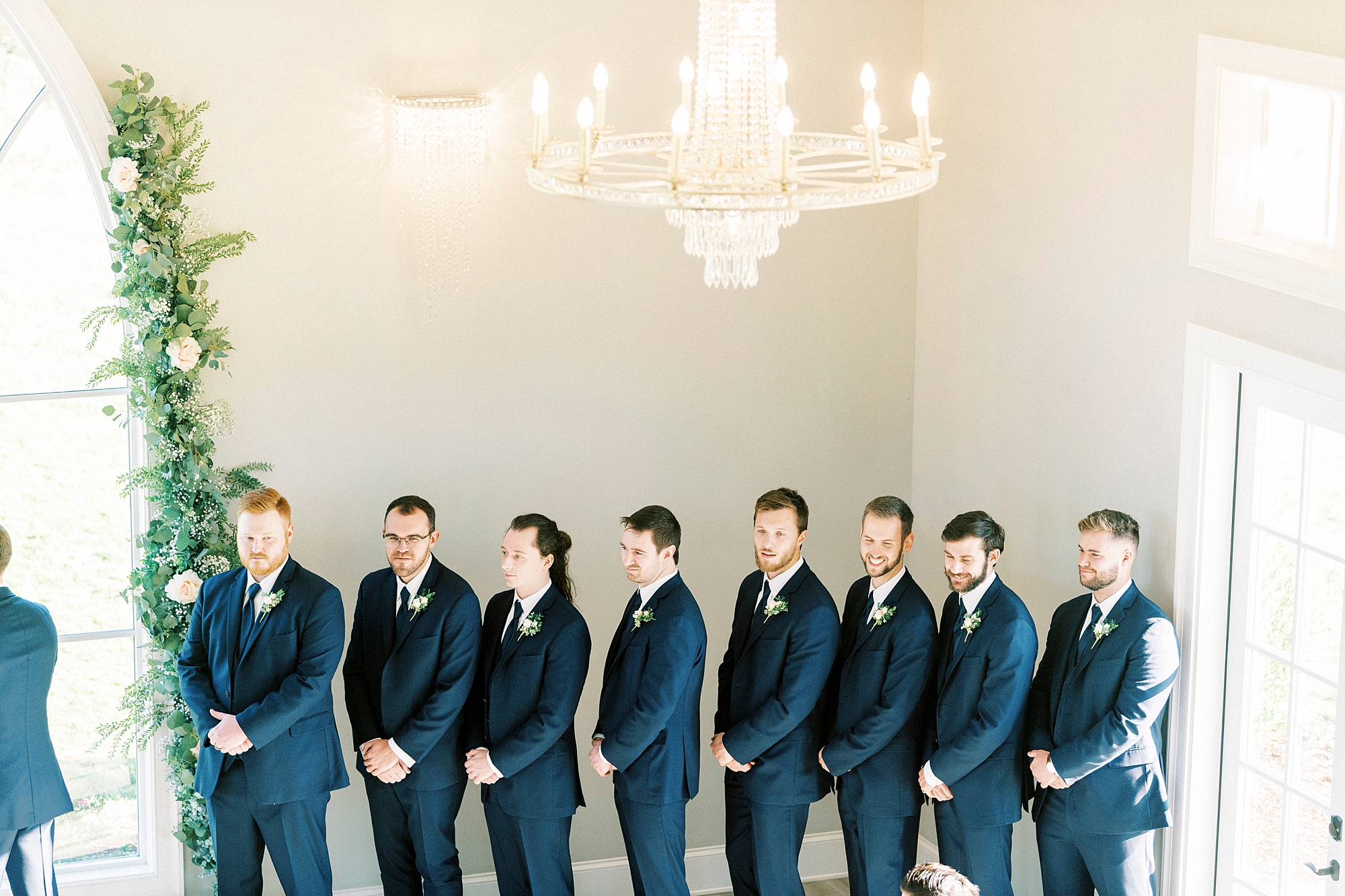 groomsmen in navy suits watch groom during wedding ceremony 