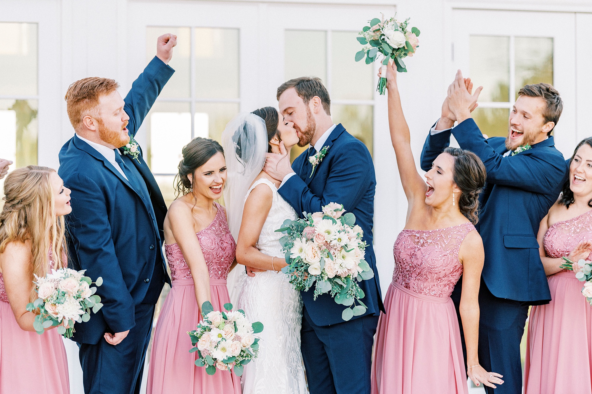 wedding party cheers while bride and groom kiss 