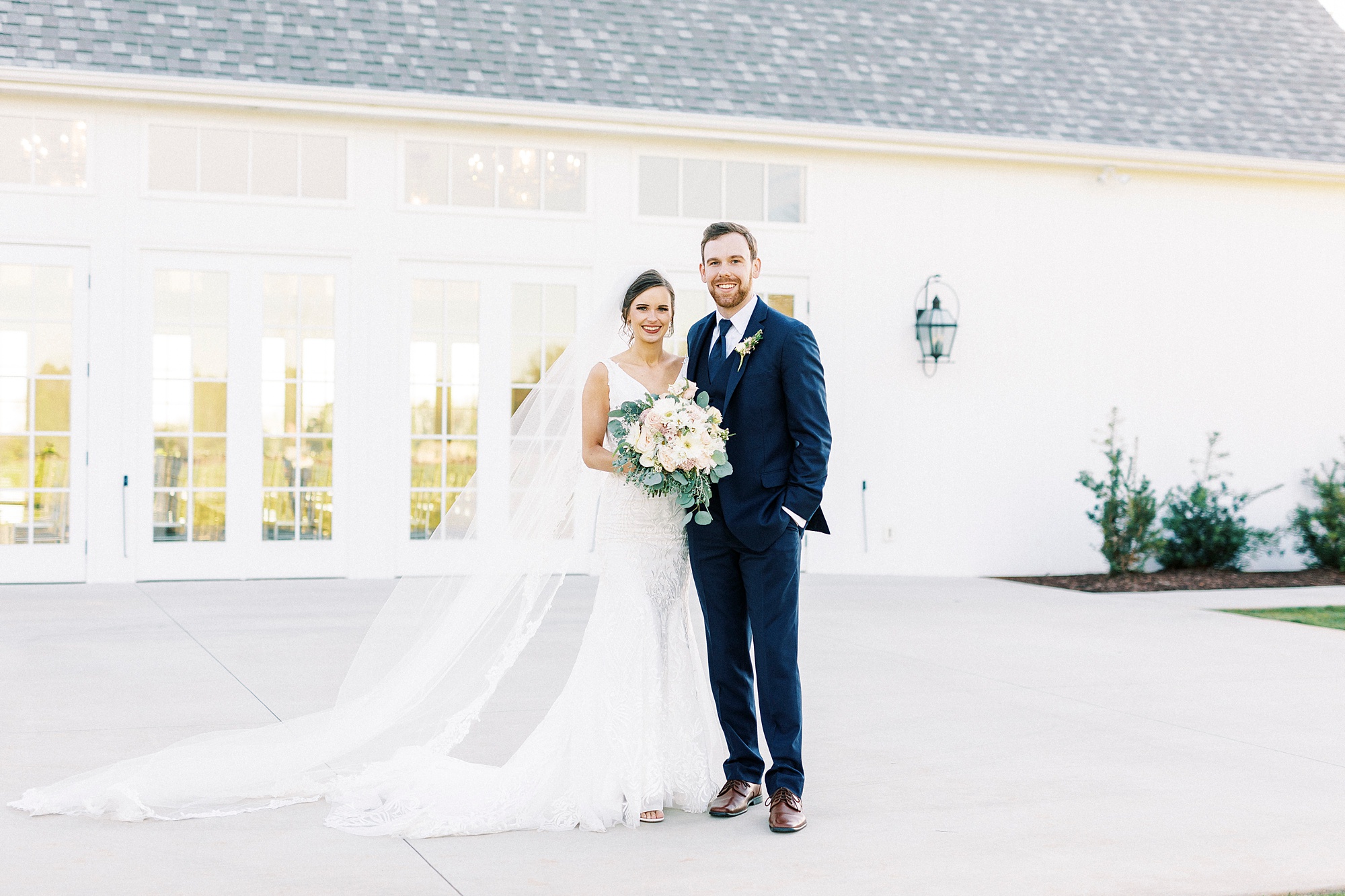 bride and groom hug outside Chickadee Hill Farms with bride's veil beside her 