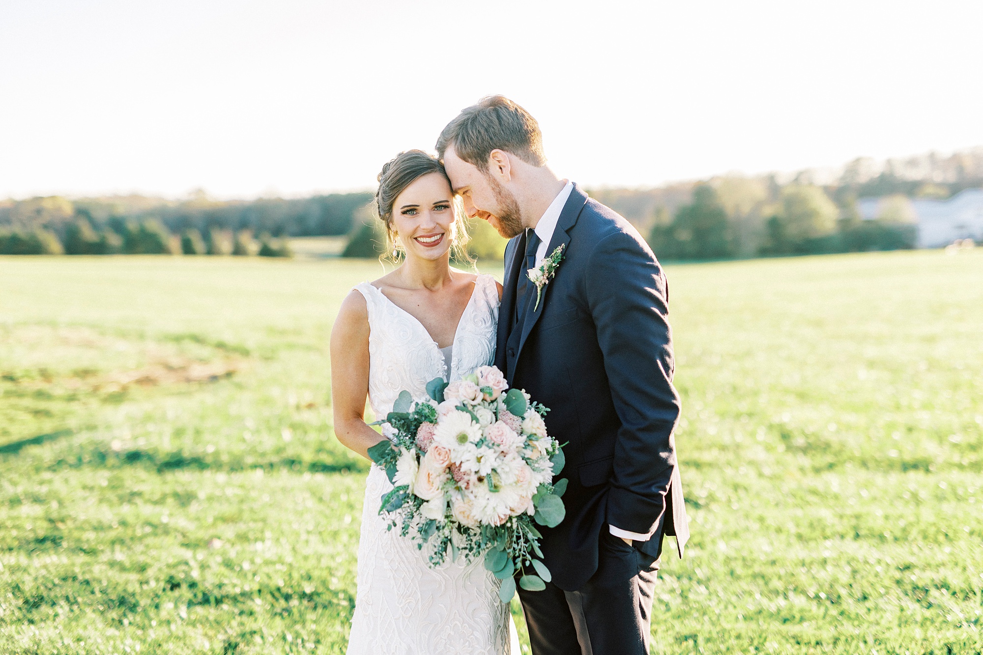groom nuzzles bride's head leaning against her in field at Chickadee Hill Farms