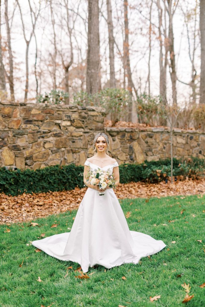 bride stands by stone wall in wedding gown with peach and ivory bouquet 