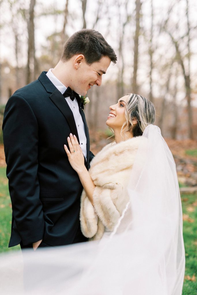 bride in light brown fur looks up at groom while veil wraps around them 