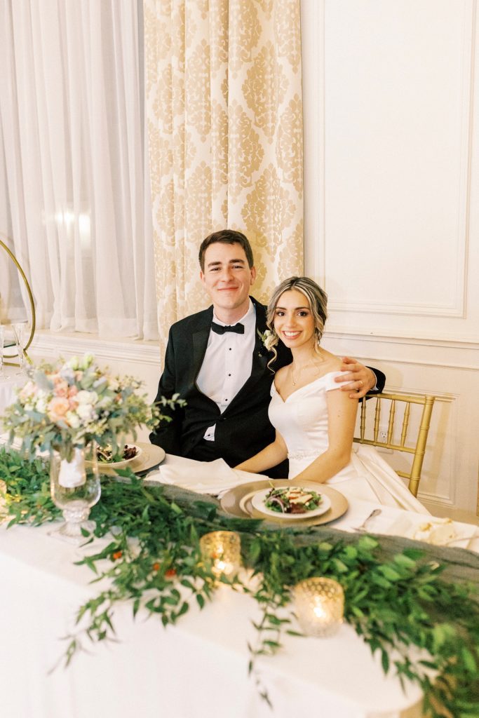 groom hugs bride to his side sitting at sweetheart table at the Hotel Concord wedding reception 