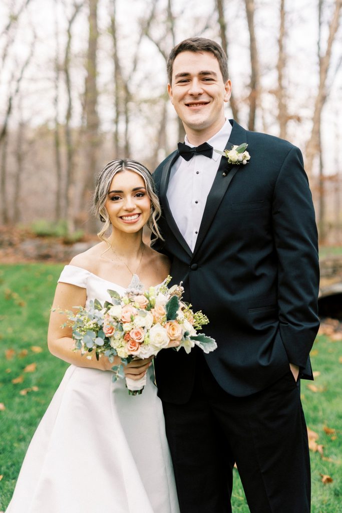 bride and groom stand together hugging on lawn in the fall 