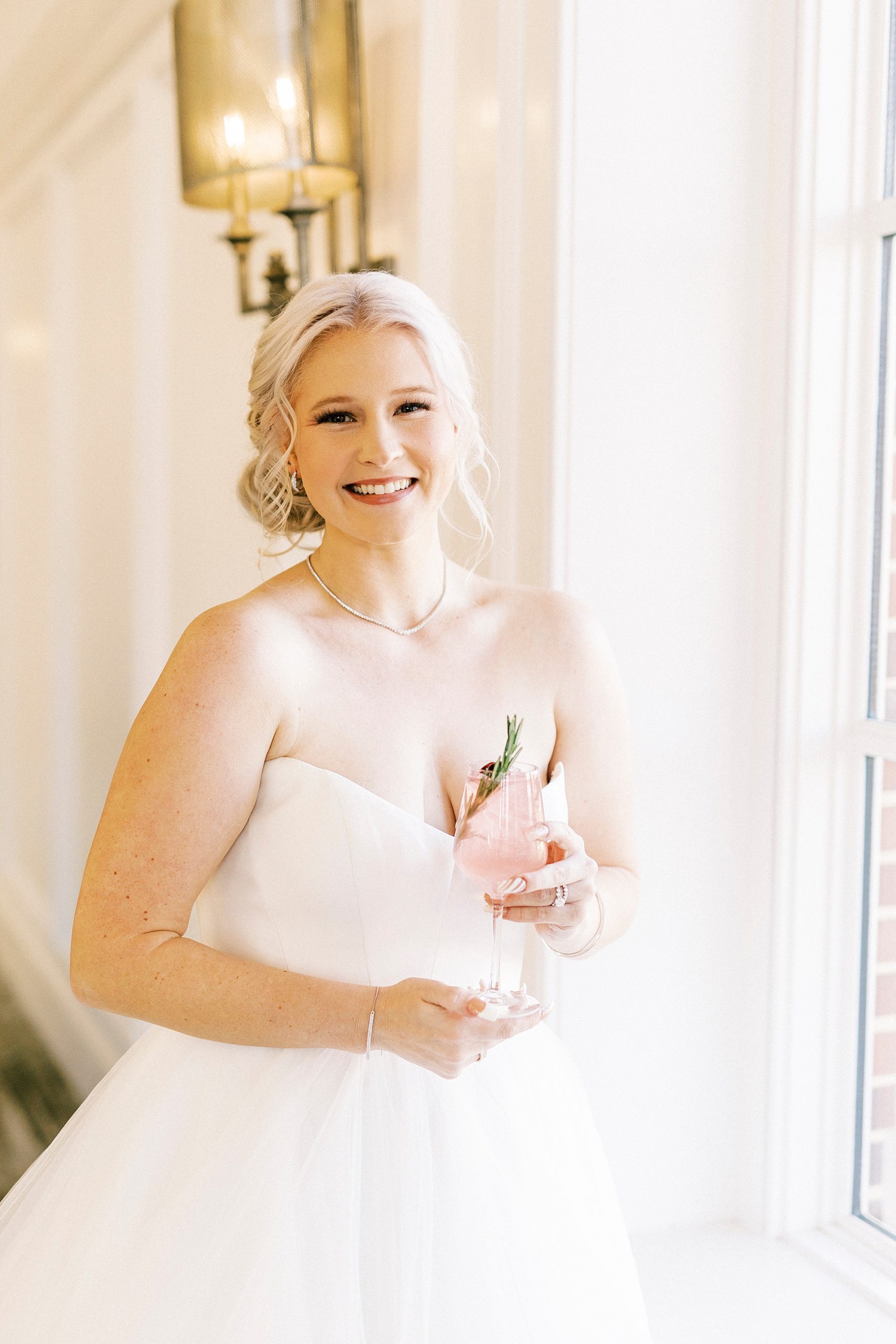 bride poses by window holding pink mixed drink