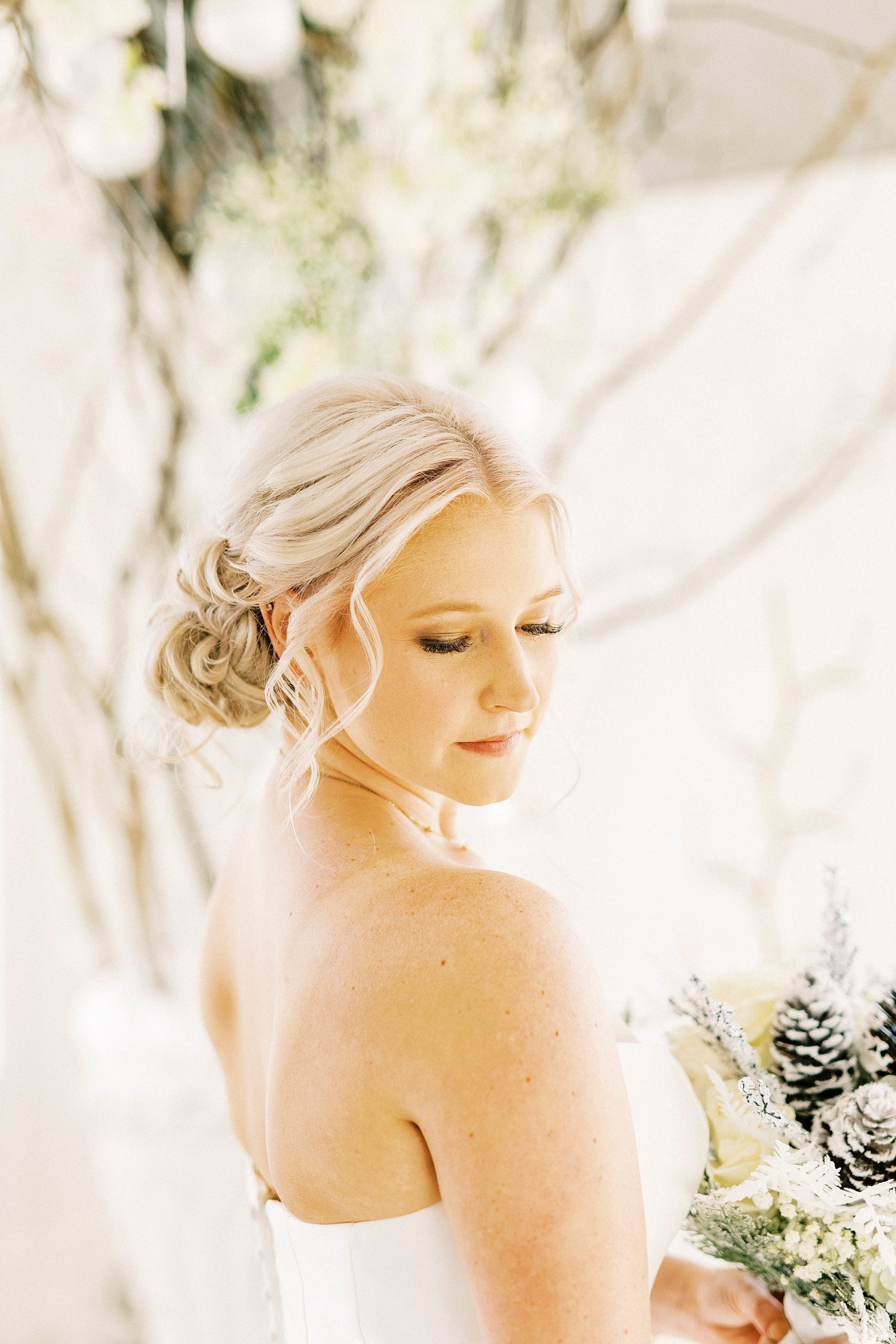 bride looks over shoulder holding bouquet with pinecone accents