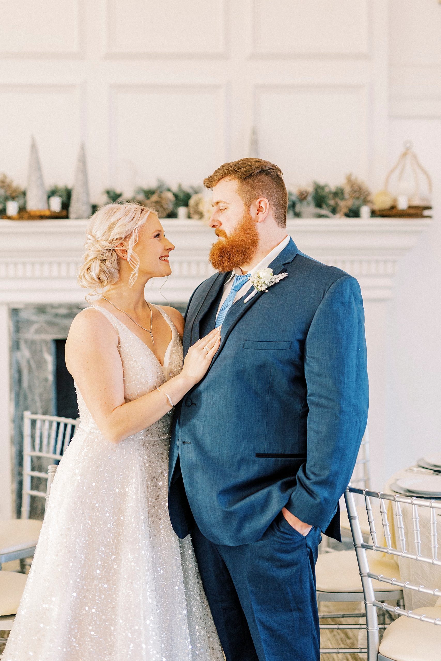 bride looks up at groom holding his lapel in front of fireplace at River Run Country Club