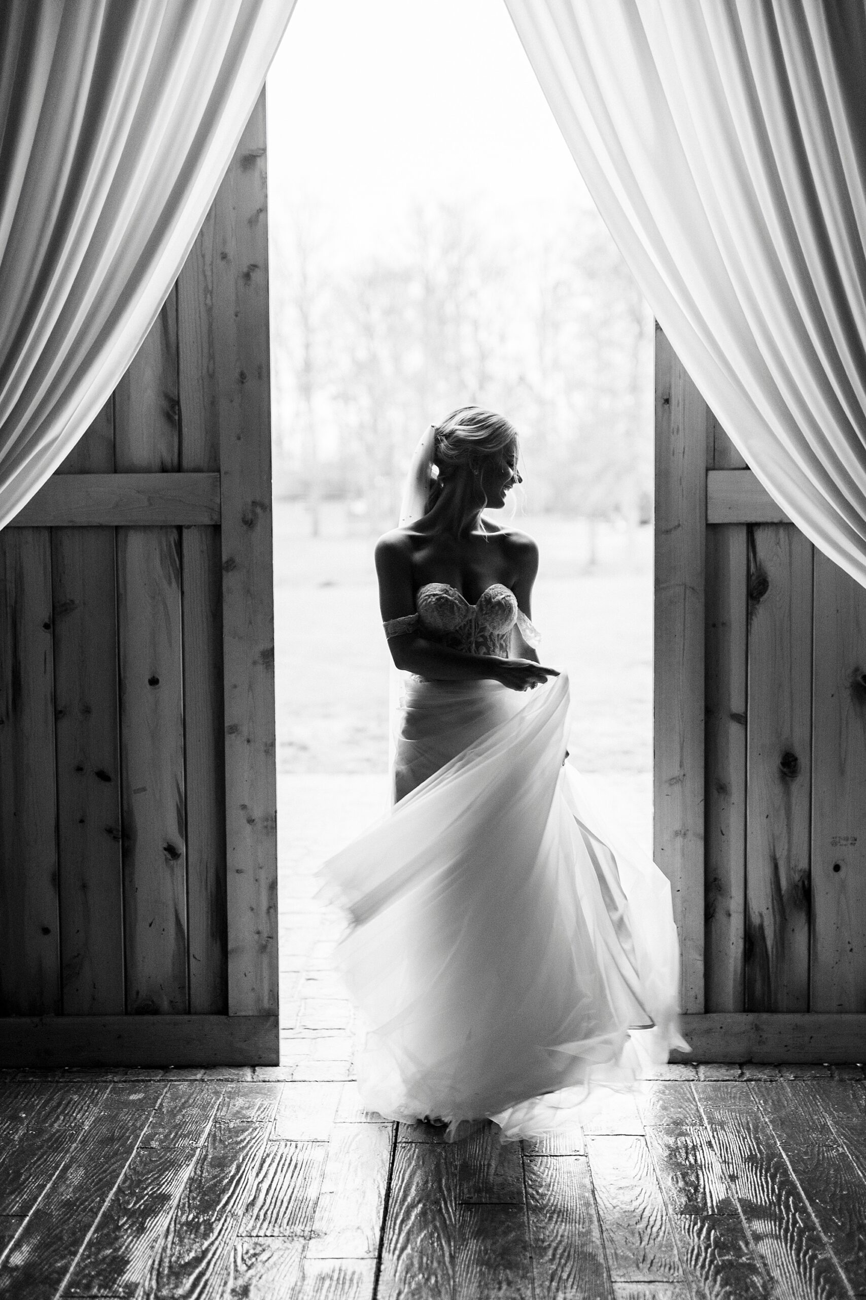 bride stands in doorway of barn looking at field at The Farmstead