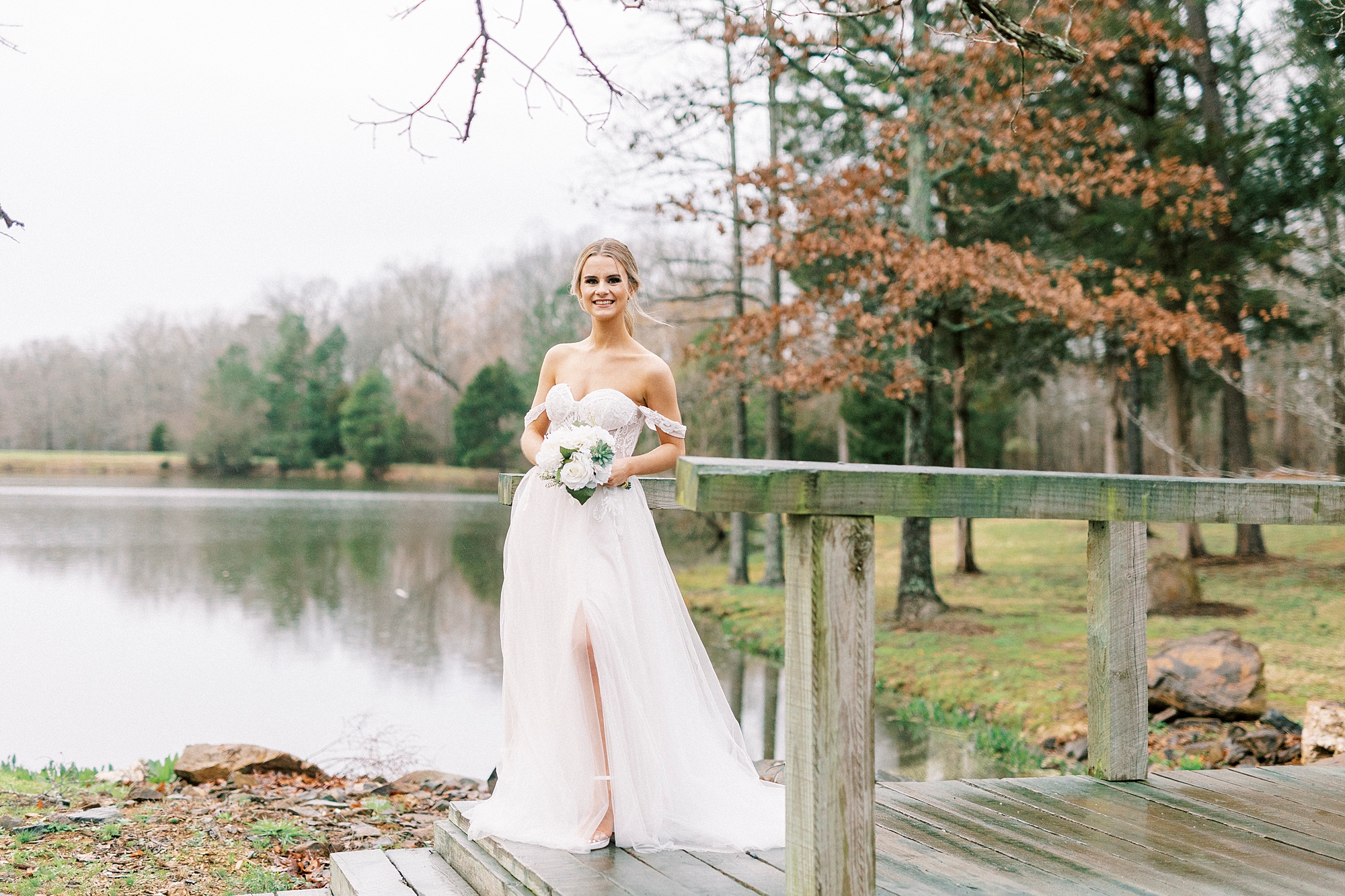 bride in wedding gown with lace corset stands on wooden dock at The Farmstead