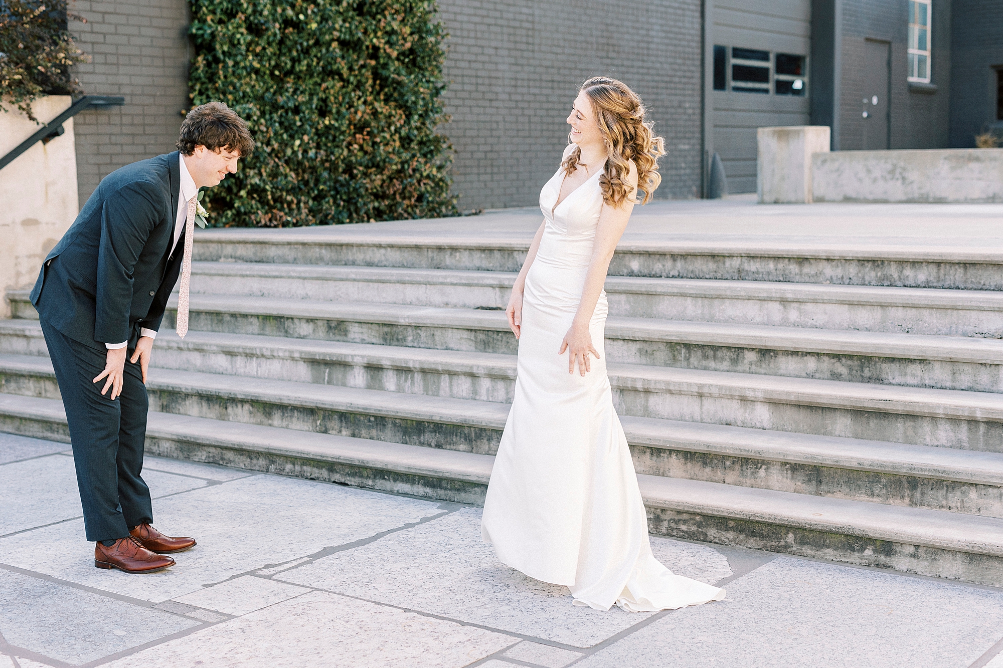 groom bends over smiling at bride during first look 