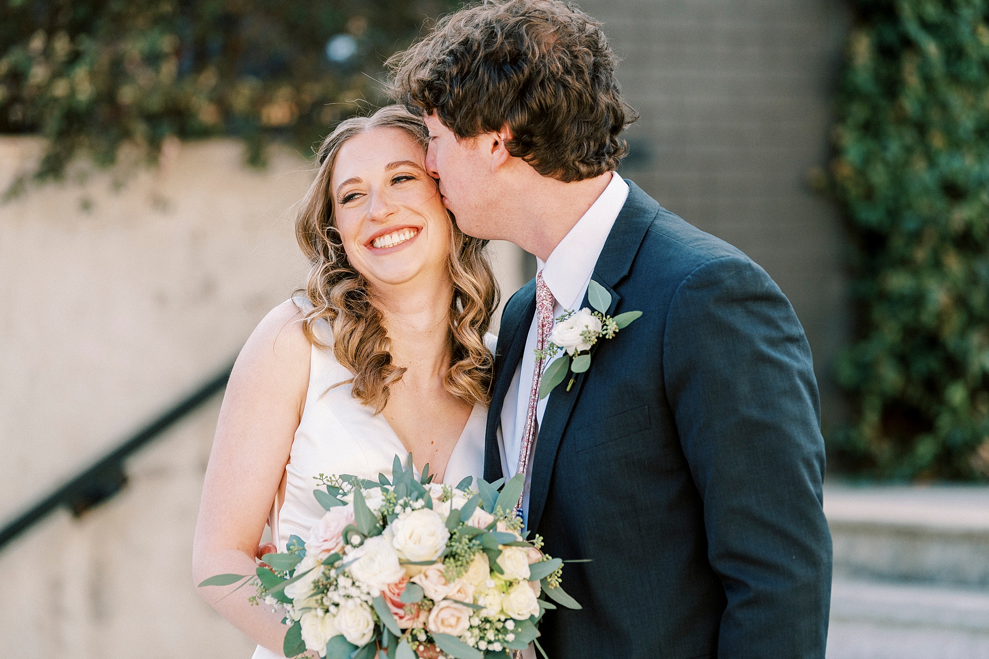 groom leans to kiss bride's cheek during portraits outside Cadillac Service Garage